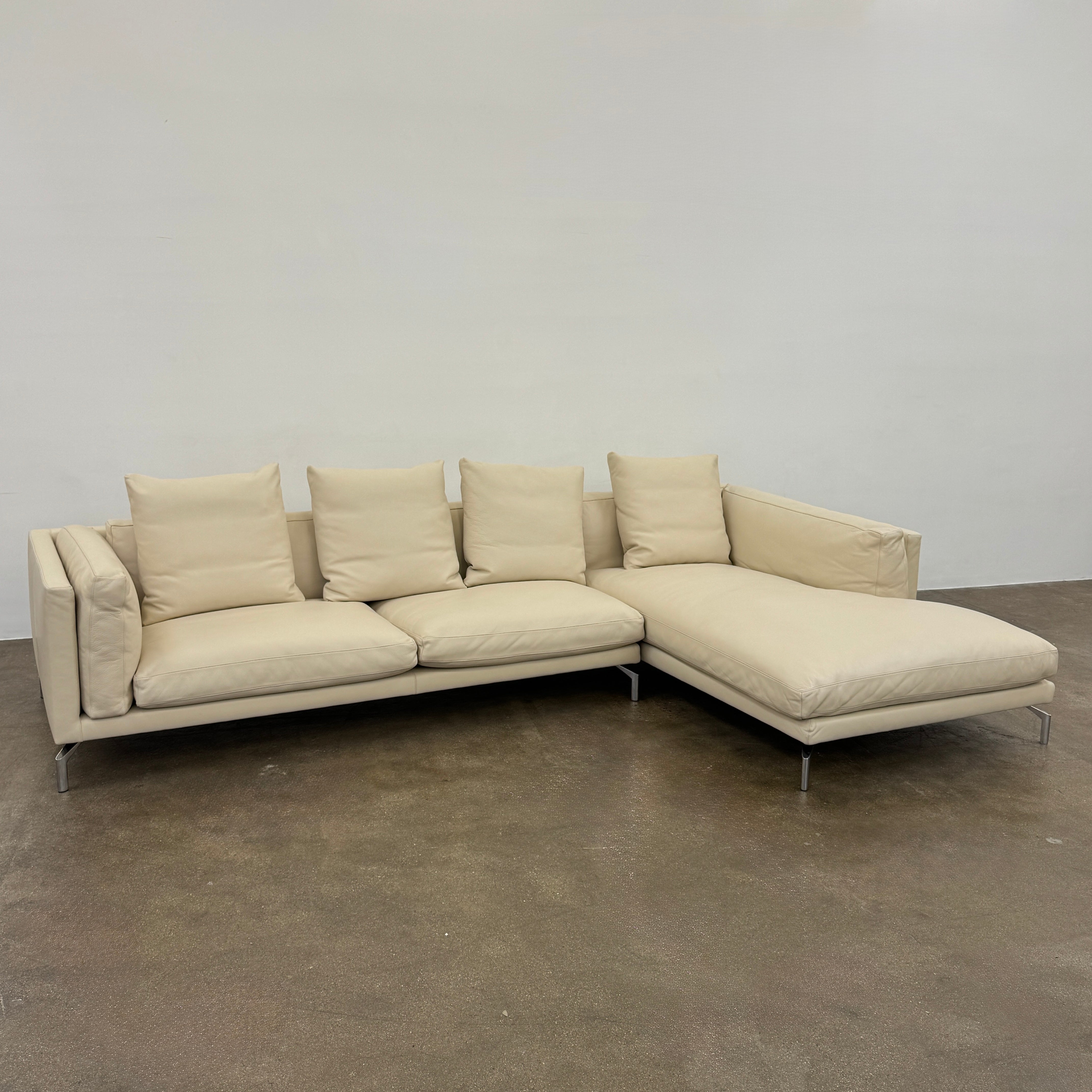 The DWR Como Sectional Sofa by DWR, in beige, features five back cushions and metal legs, showcasing Italian designer inspiration against a white background.