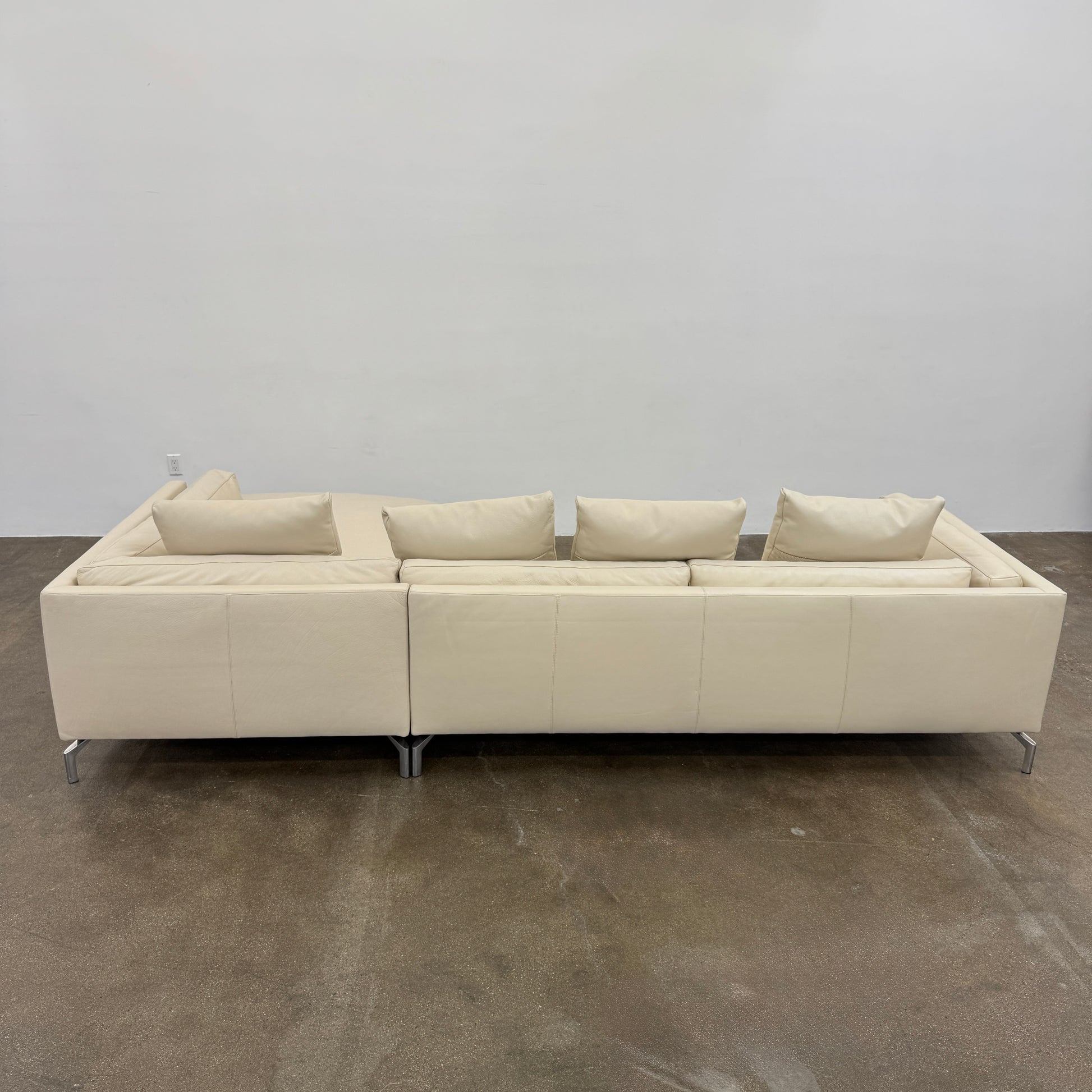The DWR Como Sectional Sofa by DWR, in beige, features five back cushions and metal legs, showcasing Italian designer inspiration against a white background.