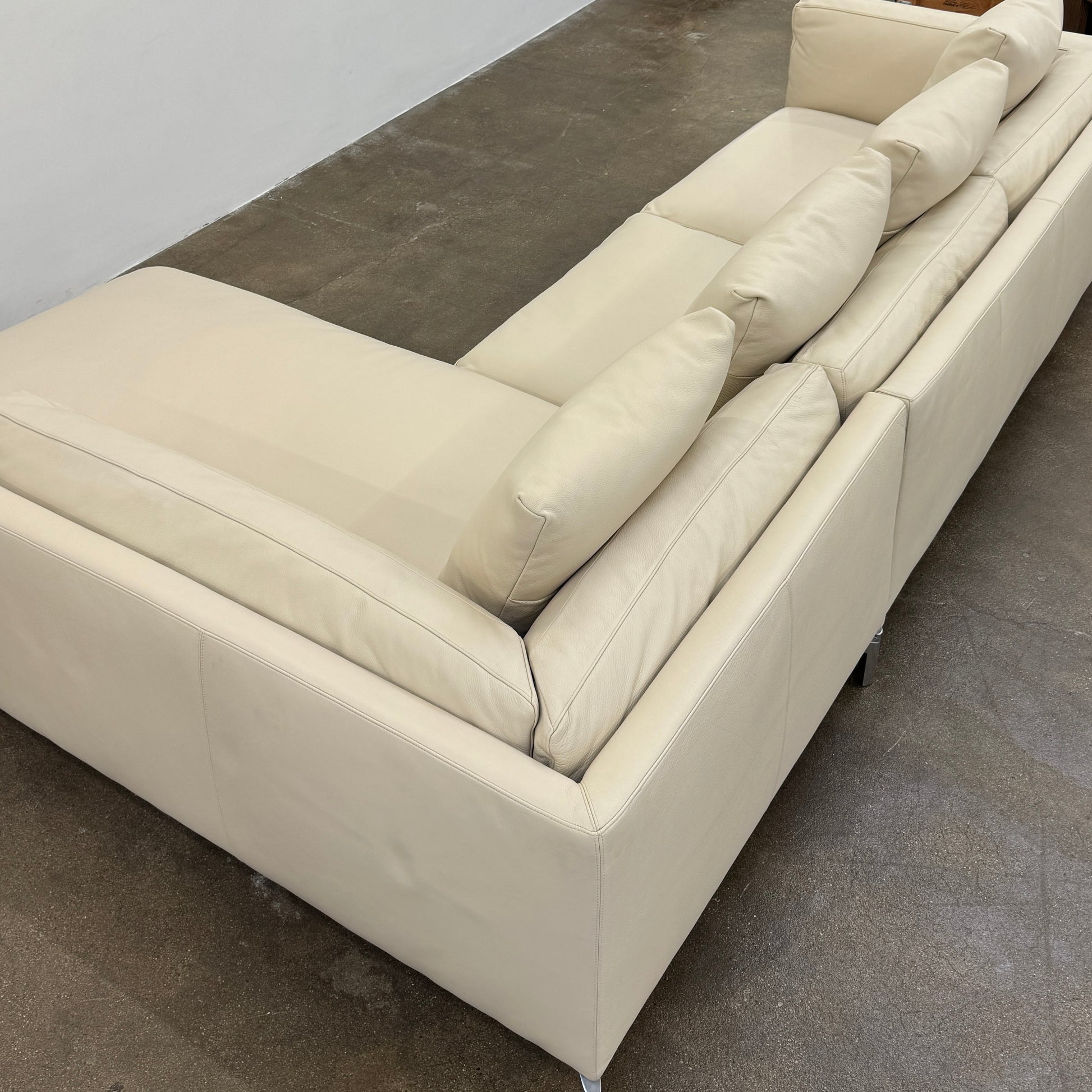 The DWR Como Sectional Sofa by DWR, in beige, features five back cushions and metal legs, showcasing Italian designer inspiration against a white background.