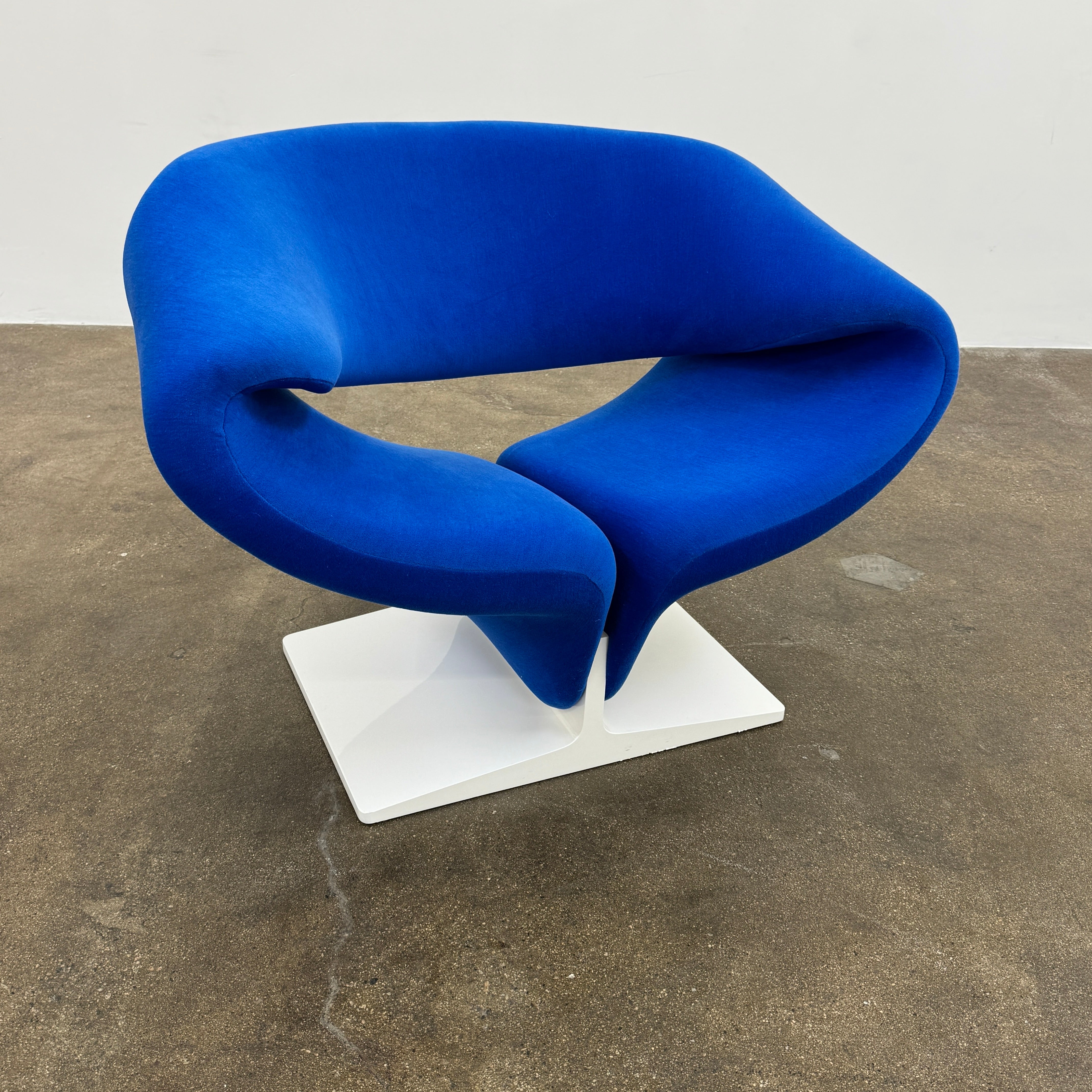 The Artifort Ribbon Lounge Chair & Ottoman by Artifort features a modern blue design with a sculptural curved backrest and split seat on a white base, seen here against a plain white background.