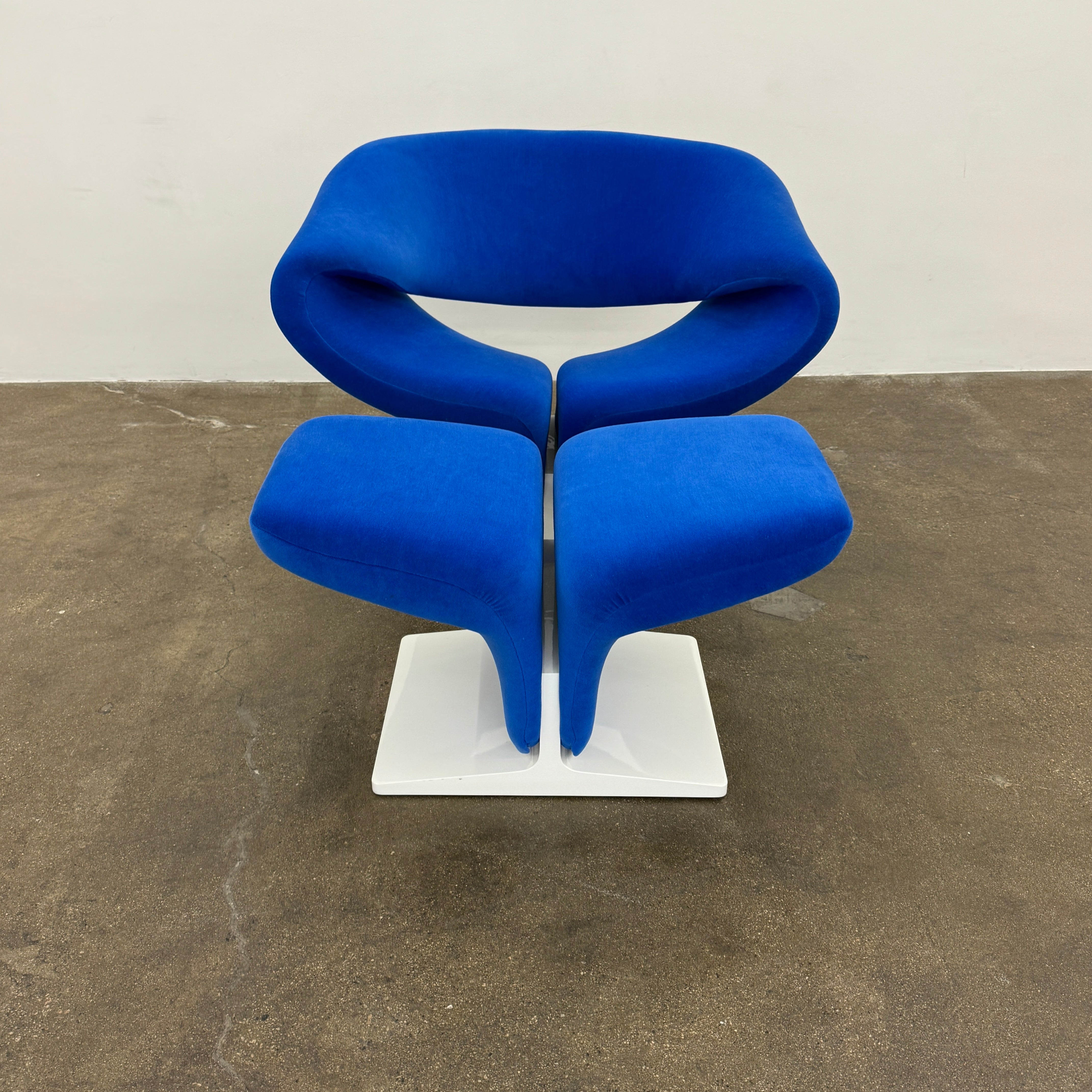 The Artifort Ribbon Lounge Chair & Ottoman by Artifort features a modern blue design with a sculptural curved backrest and split seat on a white base, seen here against a plain white background.