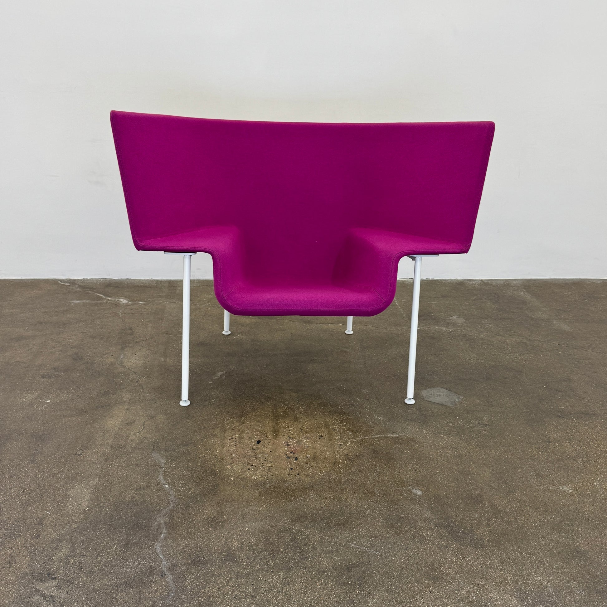The Cappellini Capo Chair by Cappellini features a modern design with bright magenta upholstery, an angular backrest, and white metal legs, set against a plain white background.