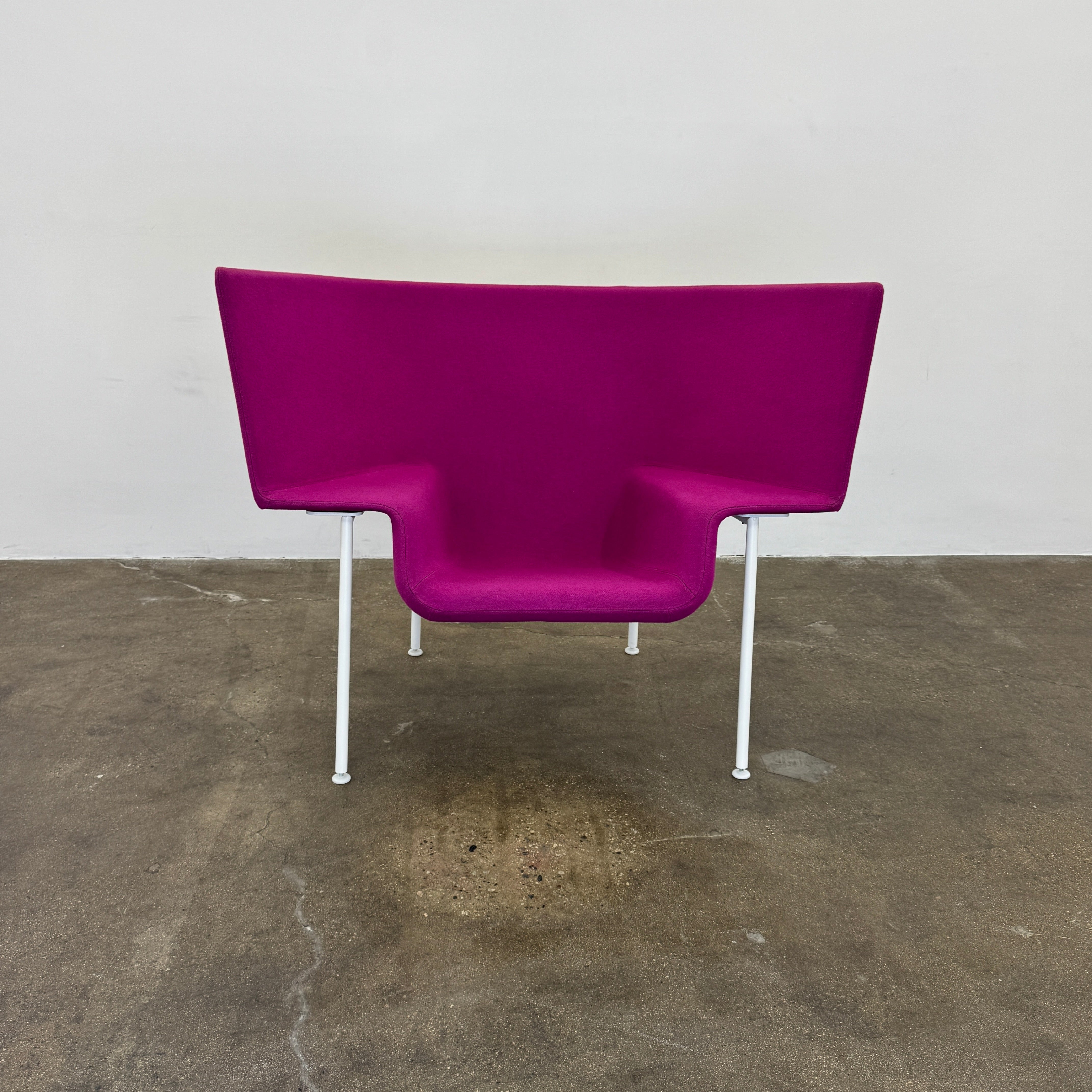 The Cappellini Capo Chair by Cappellini features a modern design with bright magenta upholstery, an angular backrest, and white metal legs, set against a plain white background.