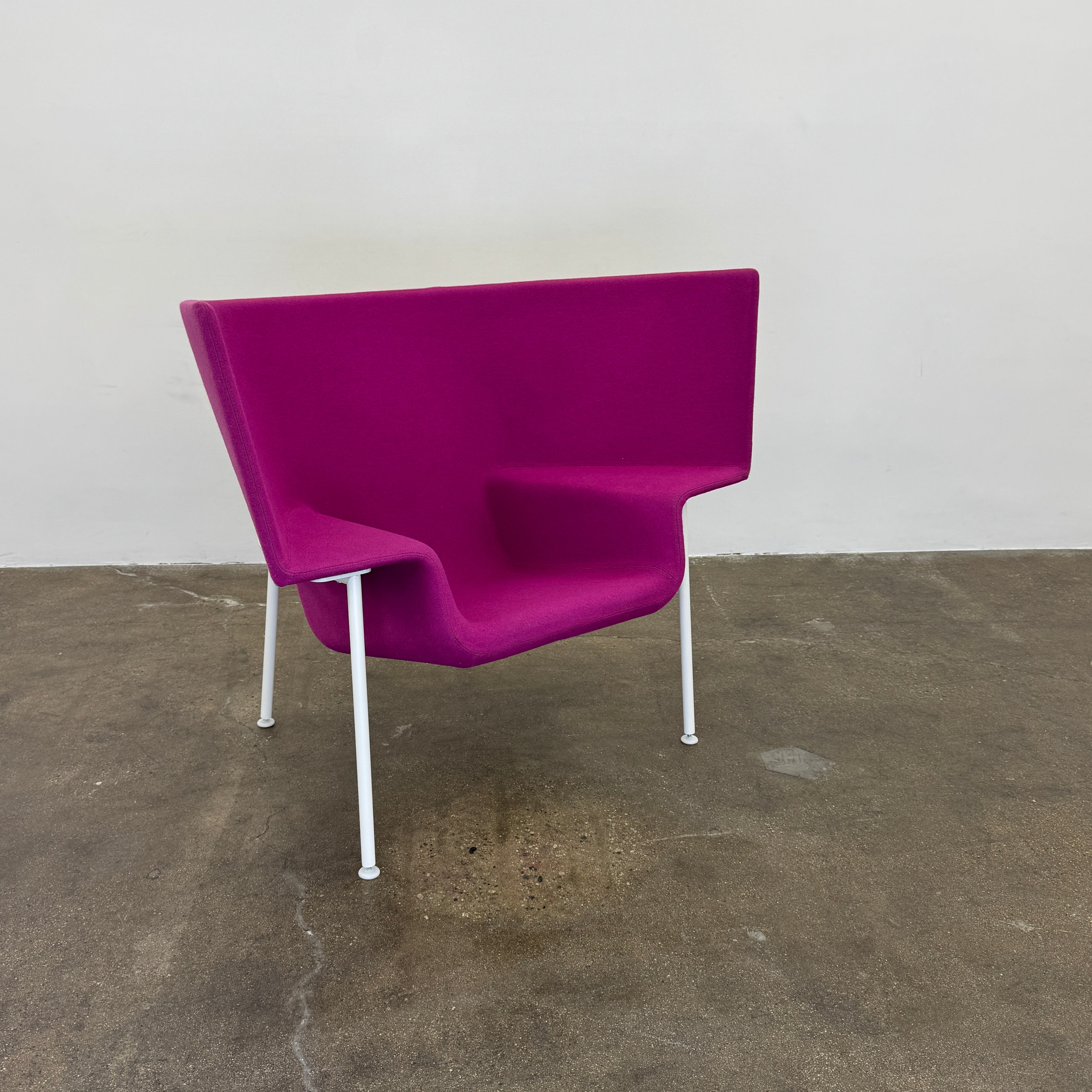 The Cappellini Capo Chair by Cappellini features a modern design with bright magenta upholstery, an angular backrest, and white metal legs, set against a plain white background.