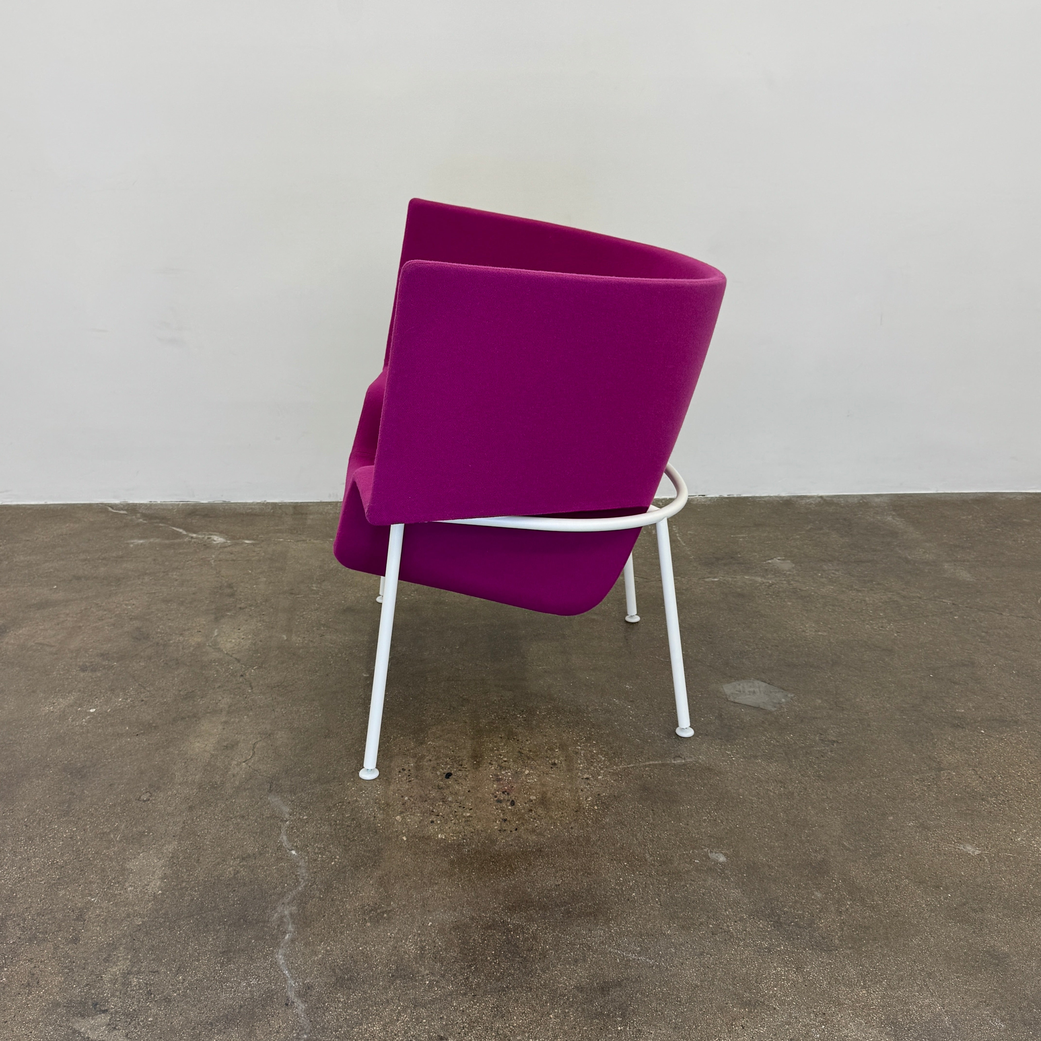 The Cappellini Capo Chair by Cappellini features a modern design with bright magenta upholstery, an angular backrest, and white metal legs, set against a plain white background.