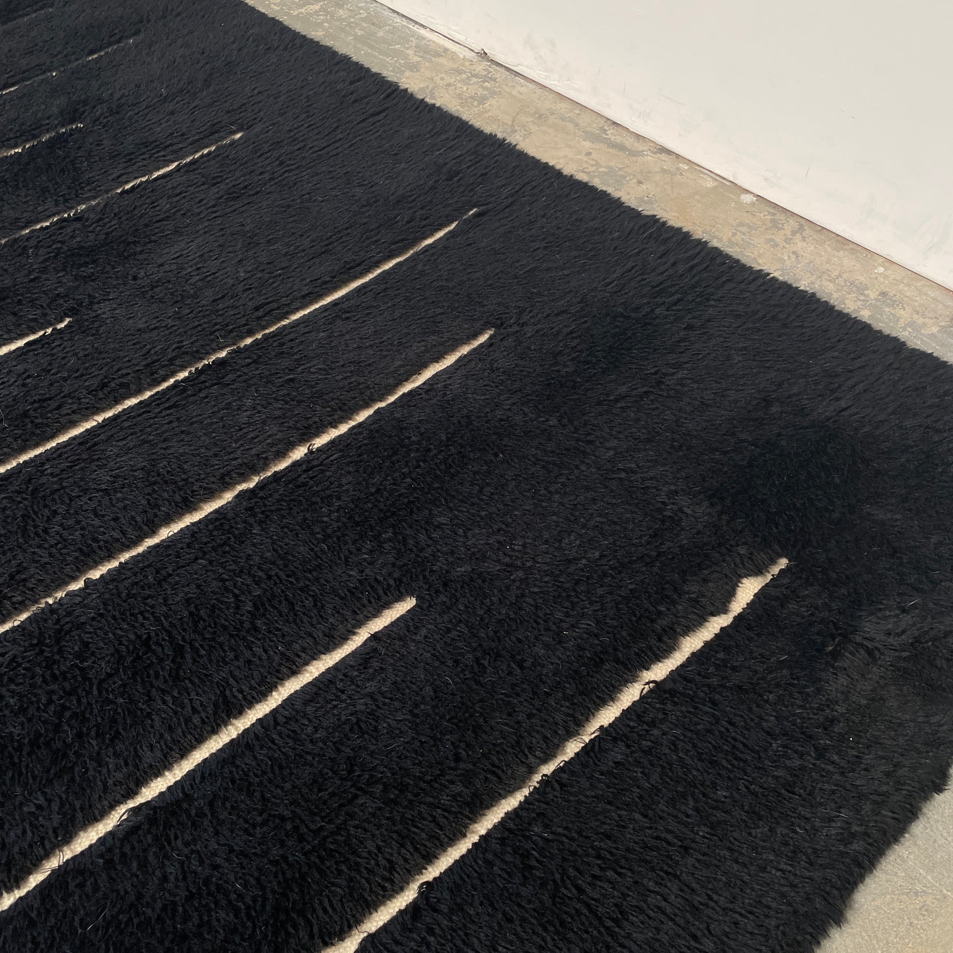 Close-up of a Woven Dilla Black & Ivory wool rug with diagonal white stitching, creating a distinct pattern on a high/low pile surface.