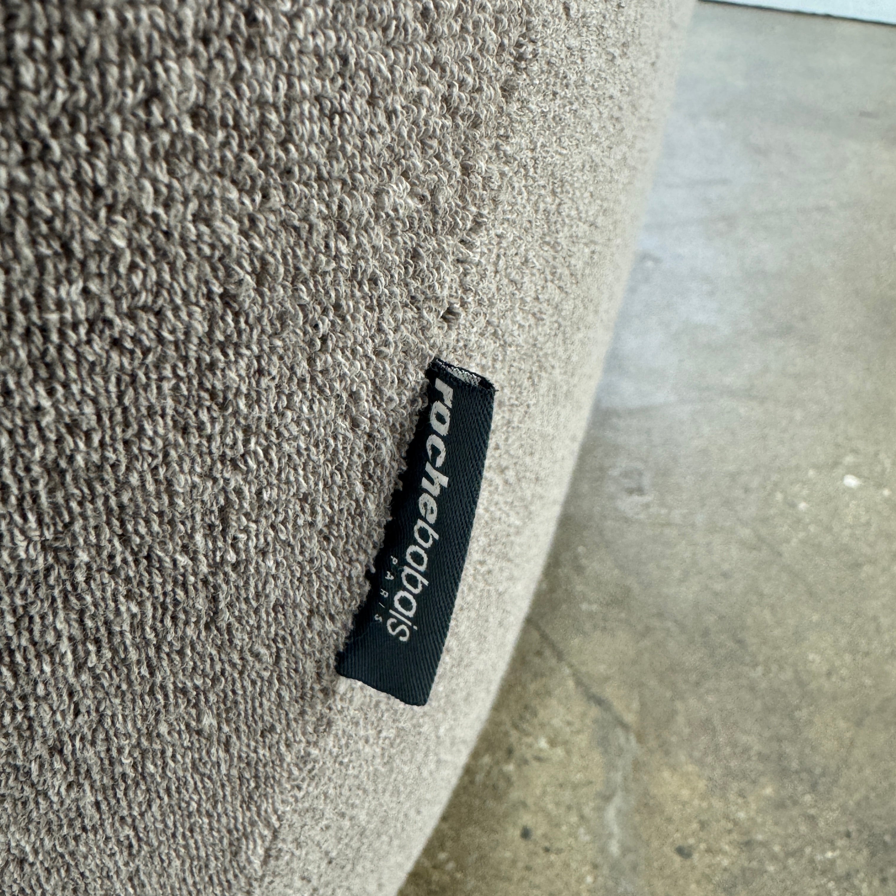 The Roche Bobois Informel Outdoor Low Back Armchair by Roche Bobois features modern, light gray upholstery with rounded arms and tufted button details for plush comfort, shown from the front on a white background.