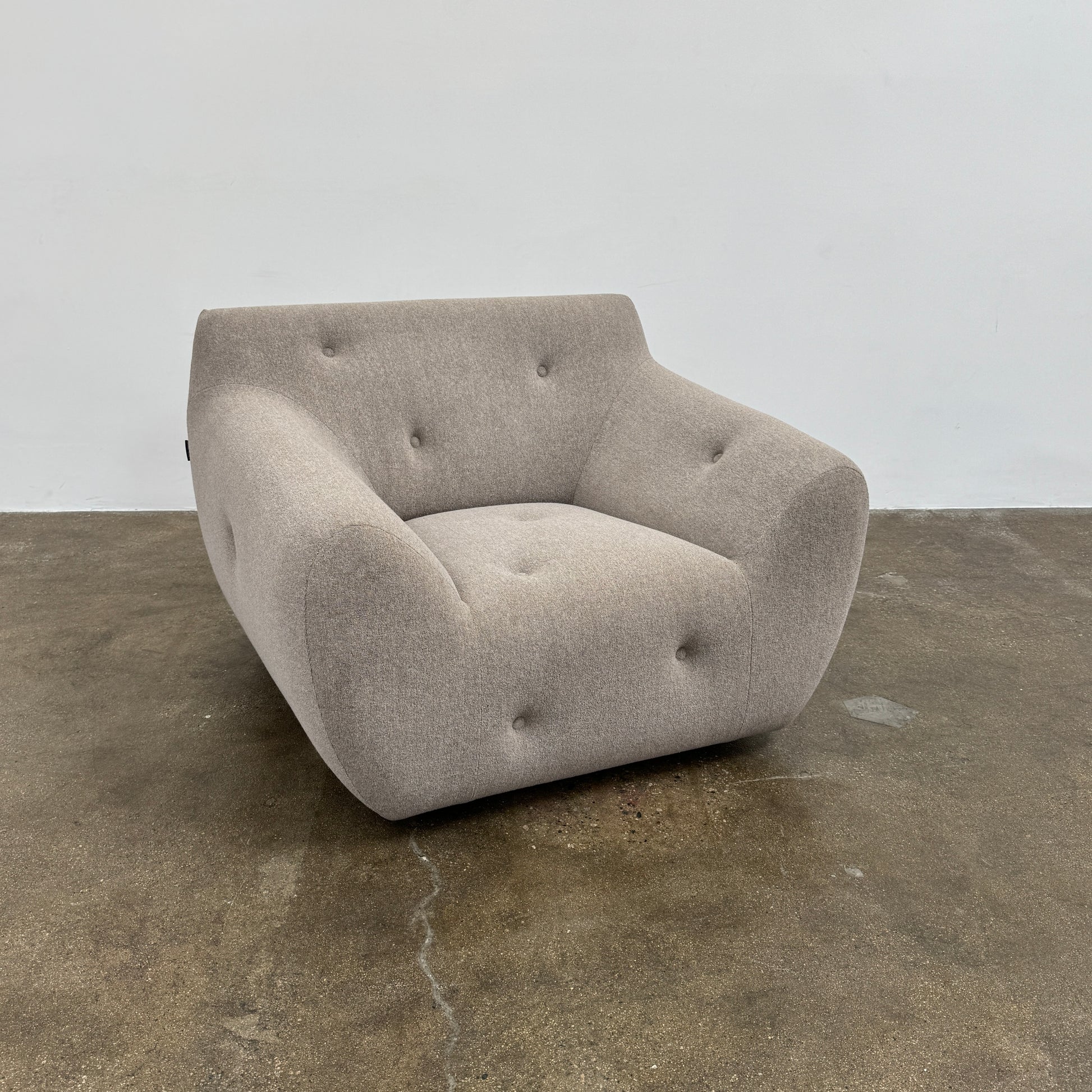 The Roche Bobois Informel Outdoor Low Back Armchair by Roche Bobois features modern, light gray upholstery with rounded arms and tufted button details for plush comfort, shown from the front on a white background.