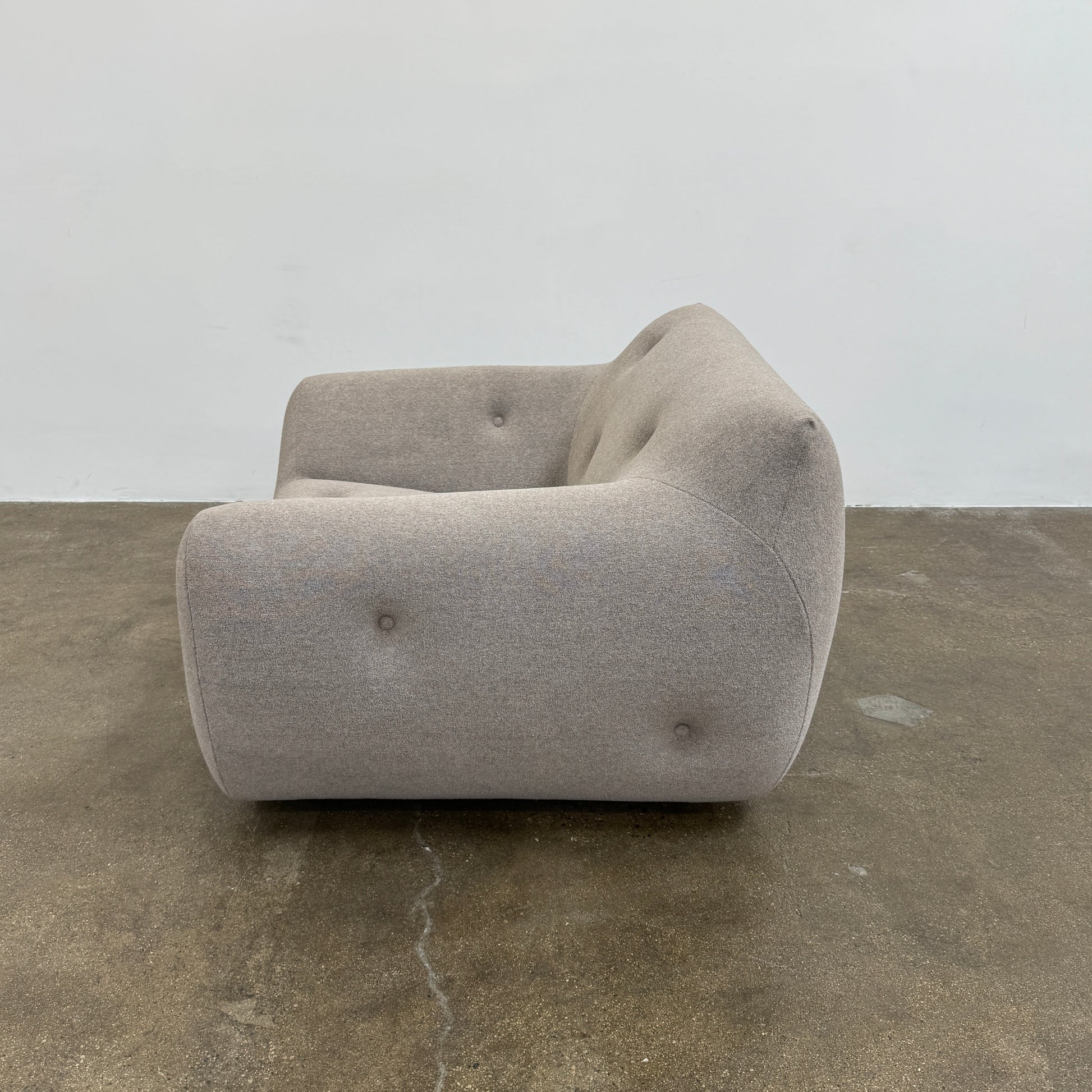 The Roche Bobois Informel Outdoor Low Back Armchair by Roche Bobois features modern, light gray upholstery with rounded arms and tufted button details for plush comfort, shown from the front on a white background.