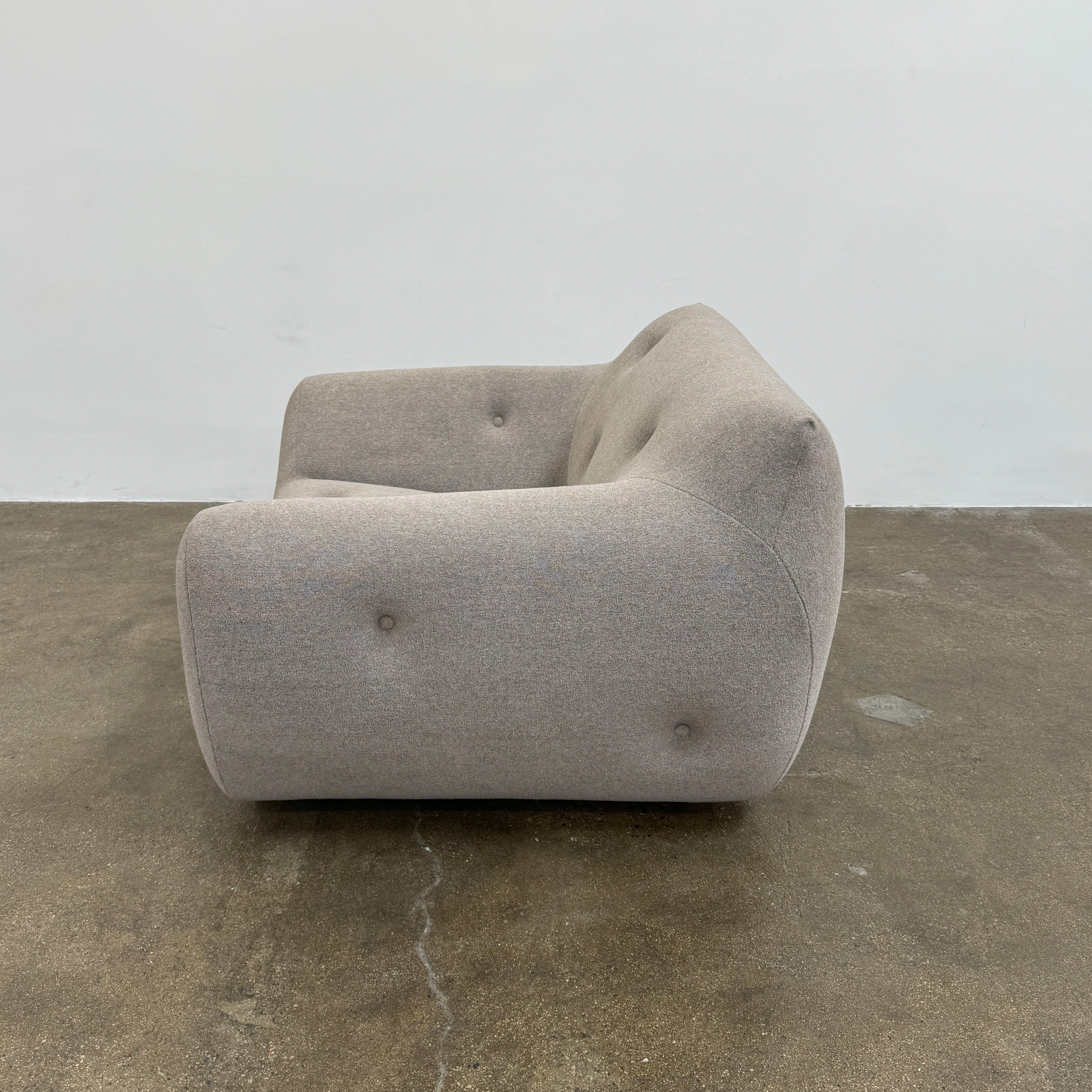 The Roche Bobois Informel Outdoor Low Back Armchair by Roche Bobois features modern, light gray upholstery with rounded arms and tufted button details for plush comfort, shown from the front on a white background.