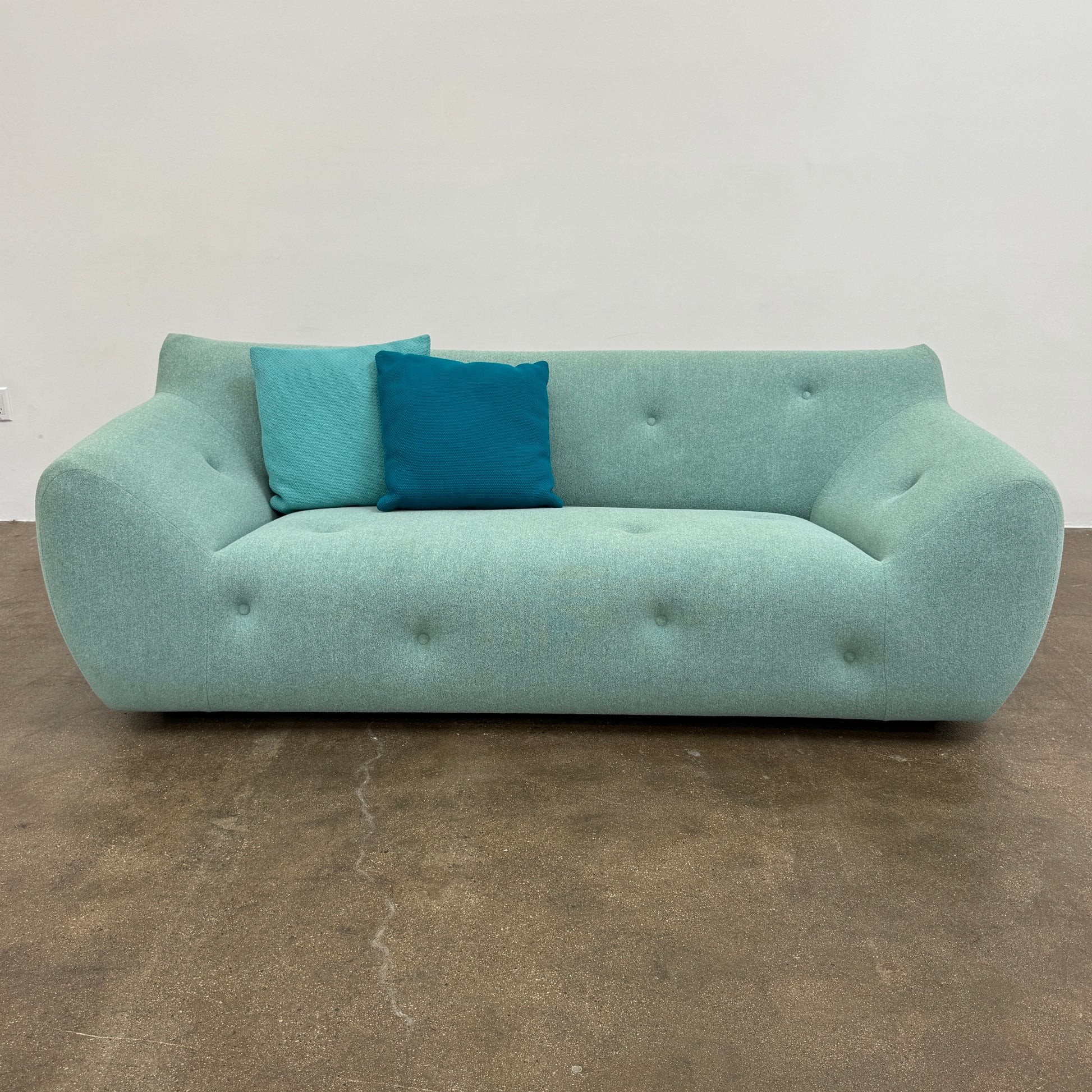 The Roche Bobois Informel Outdoor Large 3-seat Sofa Low Back features a light teal modern design with rounded edges, button-tufted details, and advanced outdoor fabric technology, inspired by Roche Bobois’s signature style.