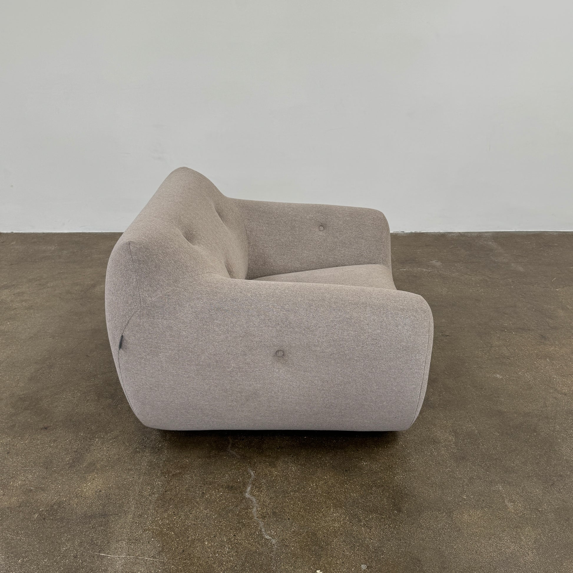 The Roche Bobois Informel Outdoor Low Back Armchair by Roche Bobois features modern, light gray upholstery with rounded arms and tufted button details for plush comfort, shown from the front on a white background.
