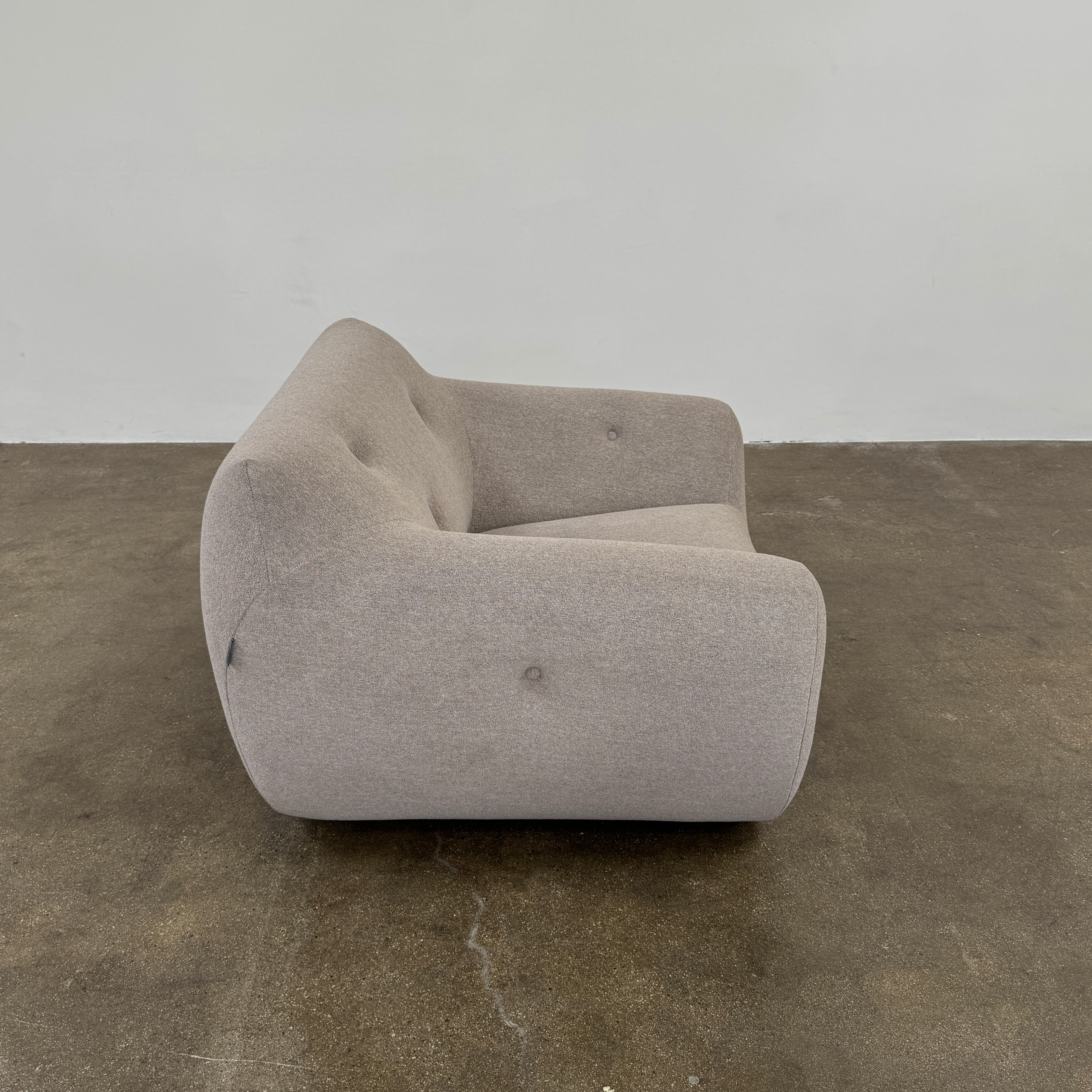 The Roche Bobois Informel Outdoor Low Back Armchair by Roche Bobois features modern, light gray upholstery with rounded arms and tufted button details for plush comfort, shown from the front on a white background.
