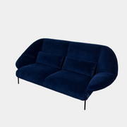The Ligne Roset Paipaï Sofa by Ligne Roset features deep blue velvet, curved edges, slim black legs, premium foam construction, and two matching rectangular cushions for a cocoon-like seat against a light background.