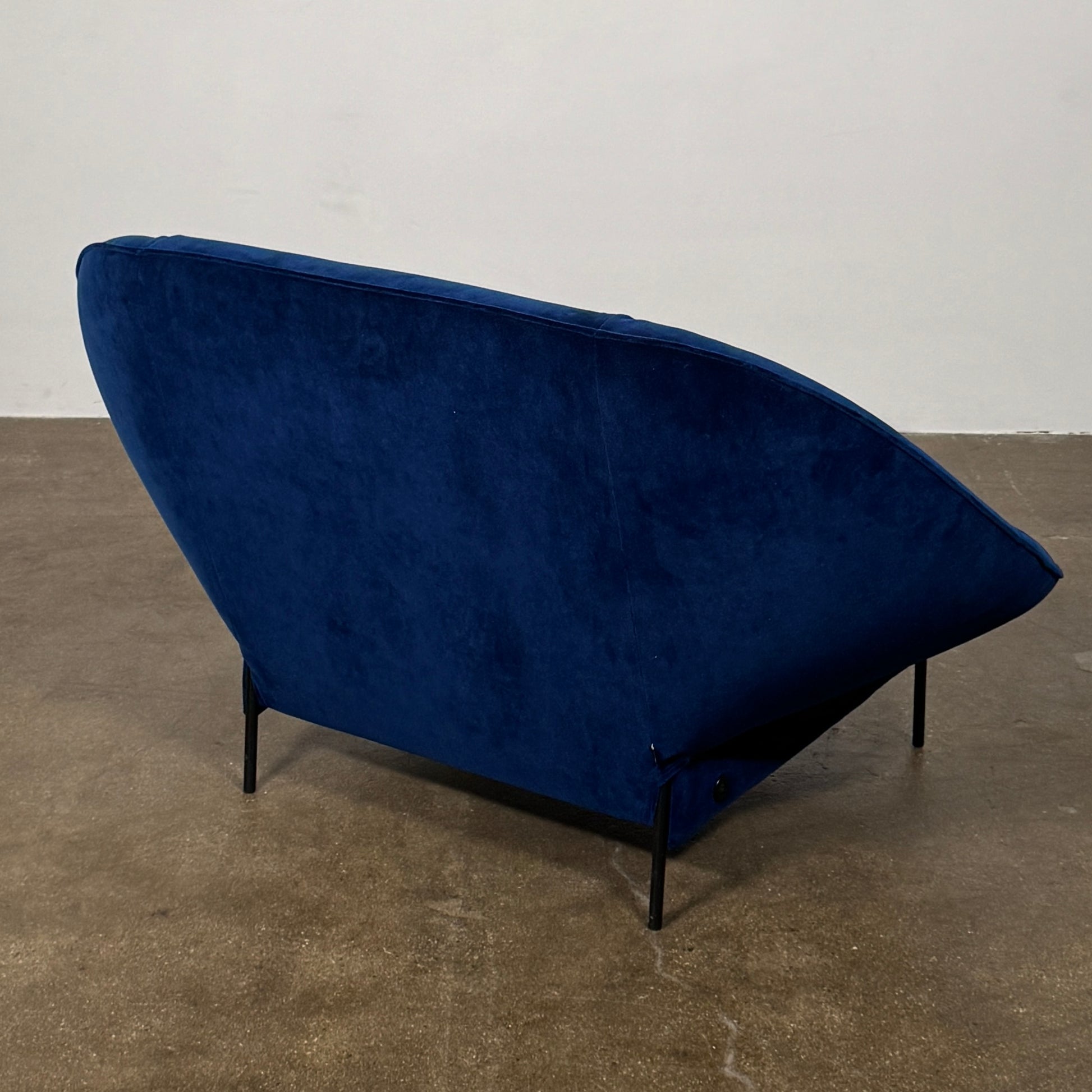 The Ligne Roset Paipai Armchair by Ligne Roset features a navy blue velvet finish, curved cocoon-like seat, matching rectangular cushion, slim black legs, and premium foam construction, displayed against a plain background.