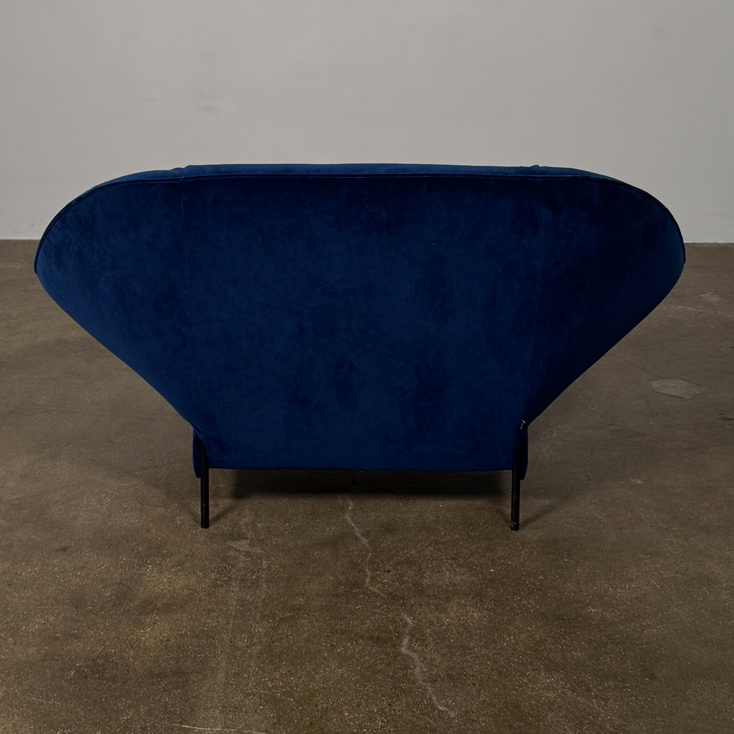 The Ligne Roset Paipai Armchair by Ligne Roset features a navy blue velvet finish, curved cocoon-like seat, matching rectangular cushion, slim black legs, and premium foam construction, displayed against a plain background.