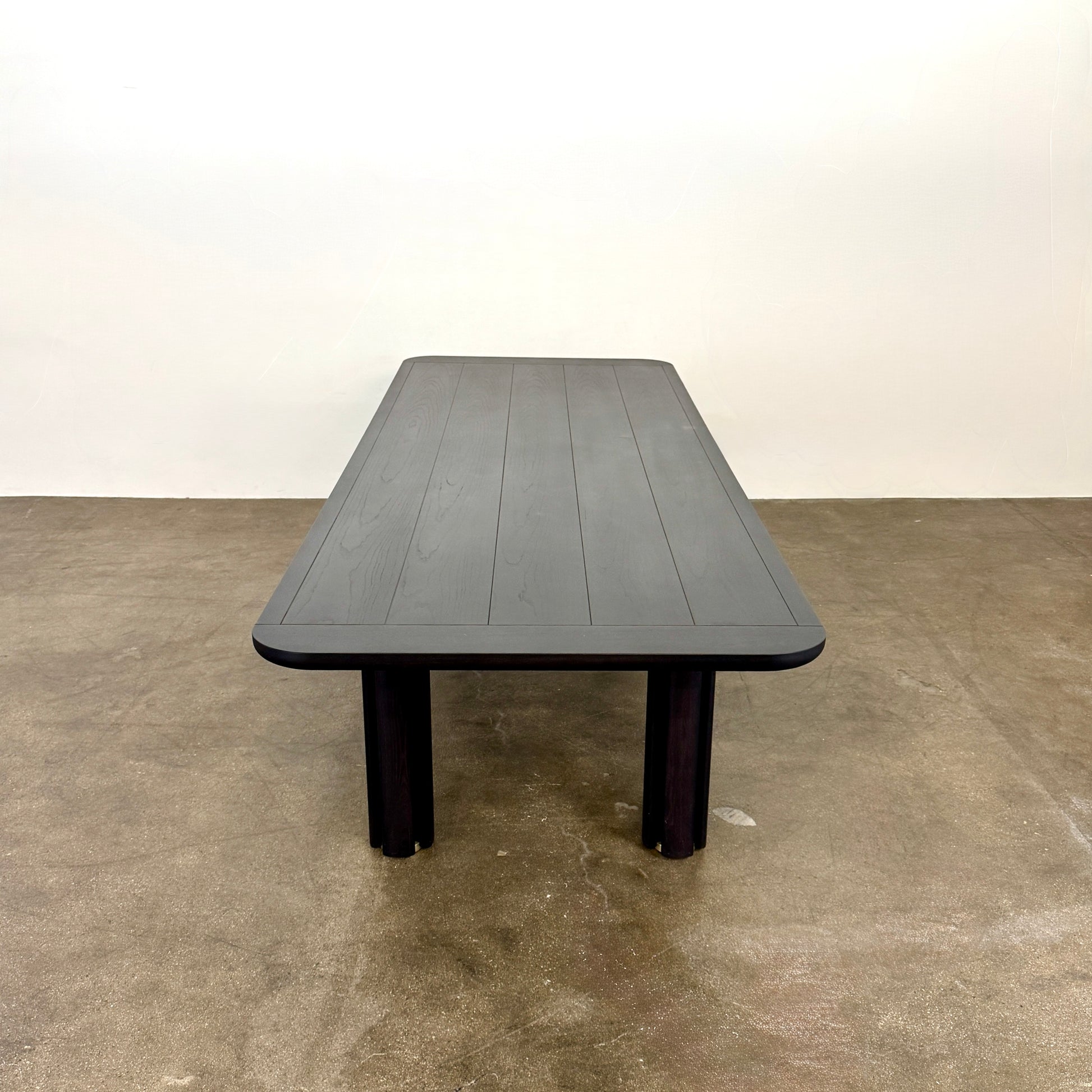 A rectangular black Porada Quadrifolgio Dining Table with rounded corners and four cylindrical legs stands on a brown floor against a plain white wall.
