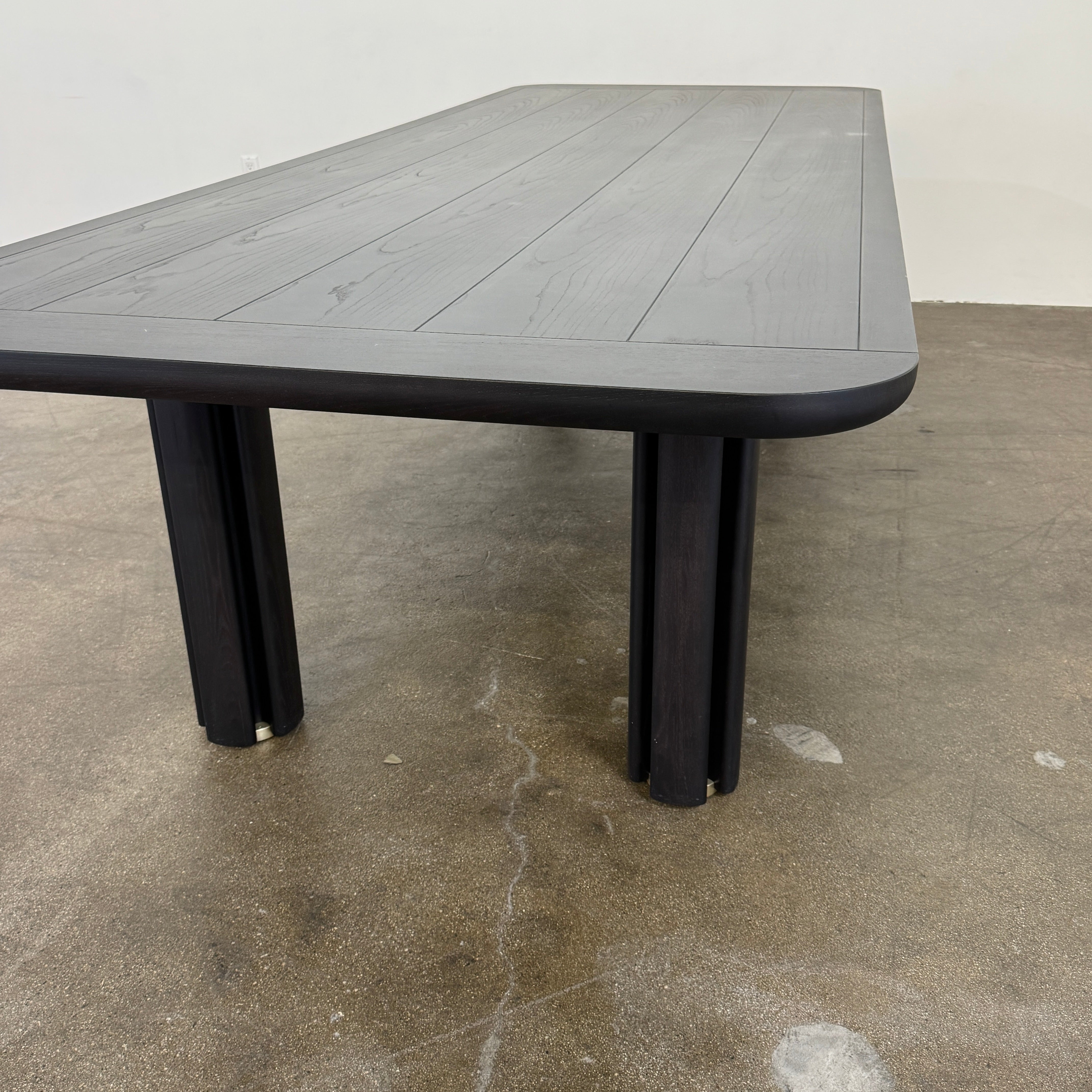 A rectangular black Porada Quadrifolgio Dining Table with rounded corners and four cylindrical legs stands on a brown floor against a plain white wall.
