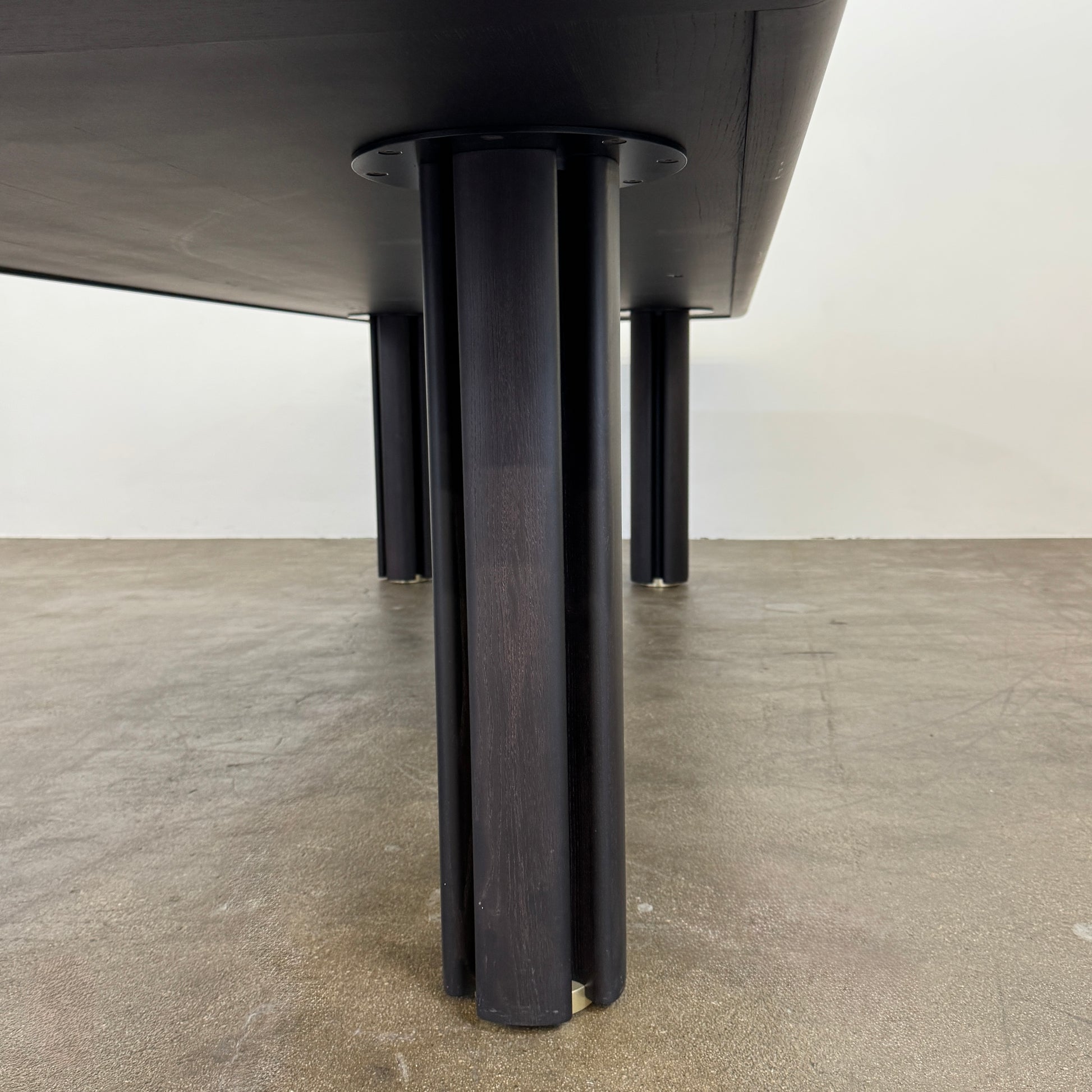 A rectangular black Porada Quadrifolgio Dining Table with rounded corners and four cylindrical legs stands on a brown floor against a plain white wall.