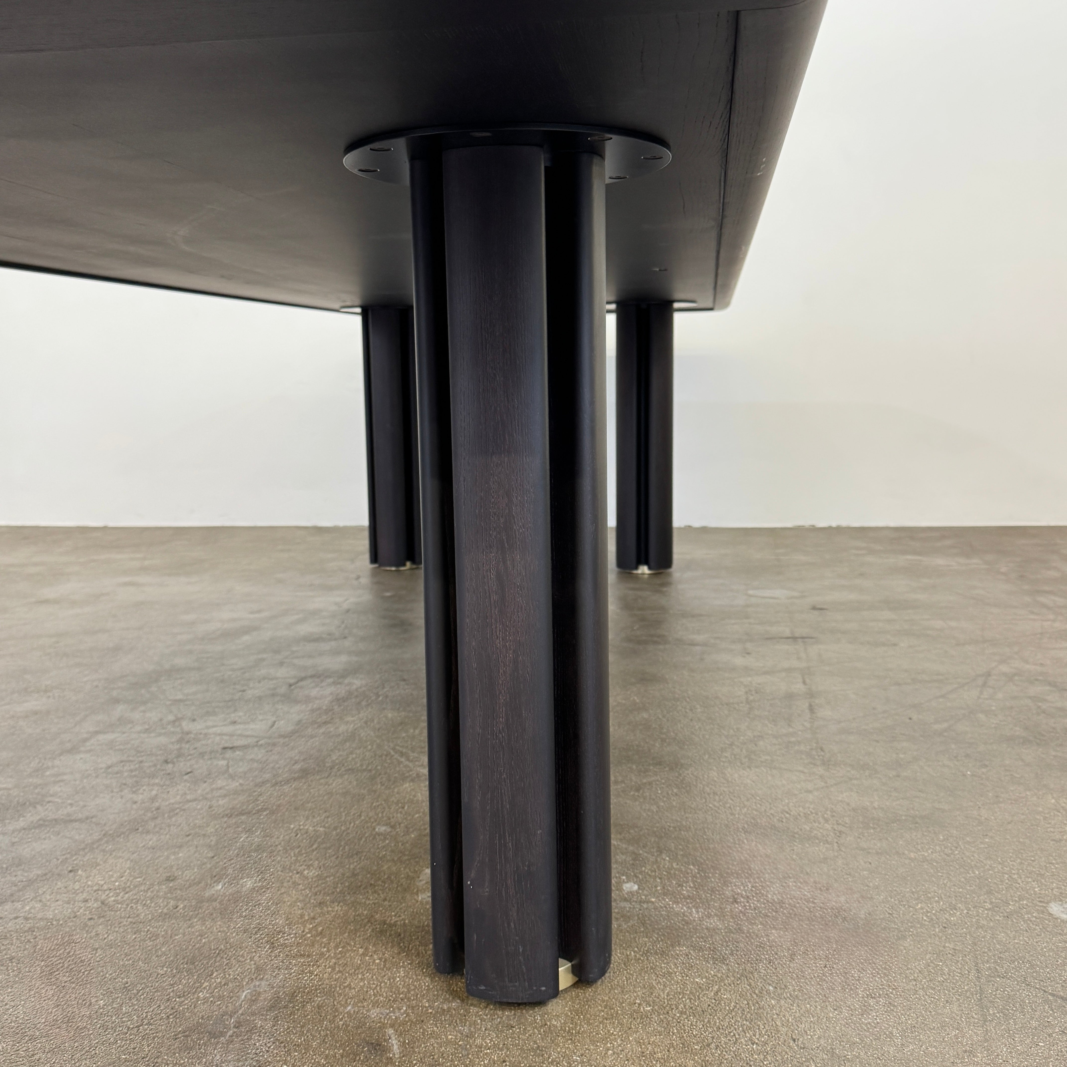 A rectangular black Porada Quadrifolgio Dining Table with rounded corners and four cylindrical legs stands on a brown floor against a plain white wall.