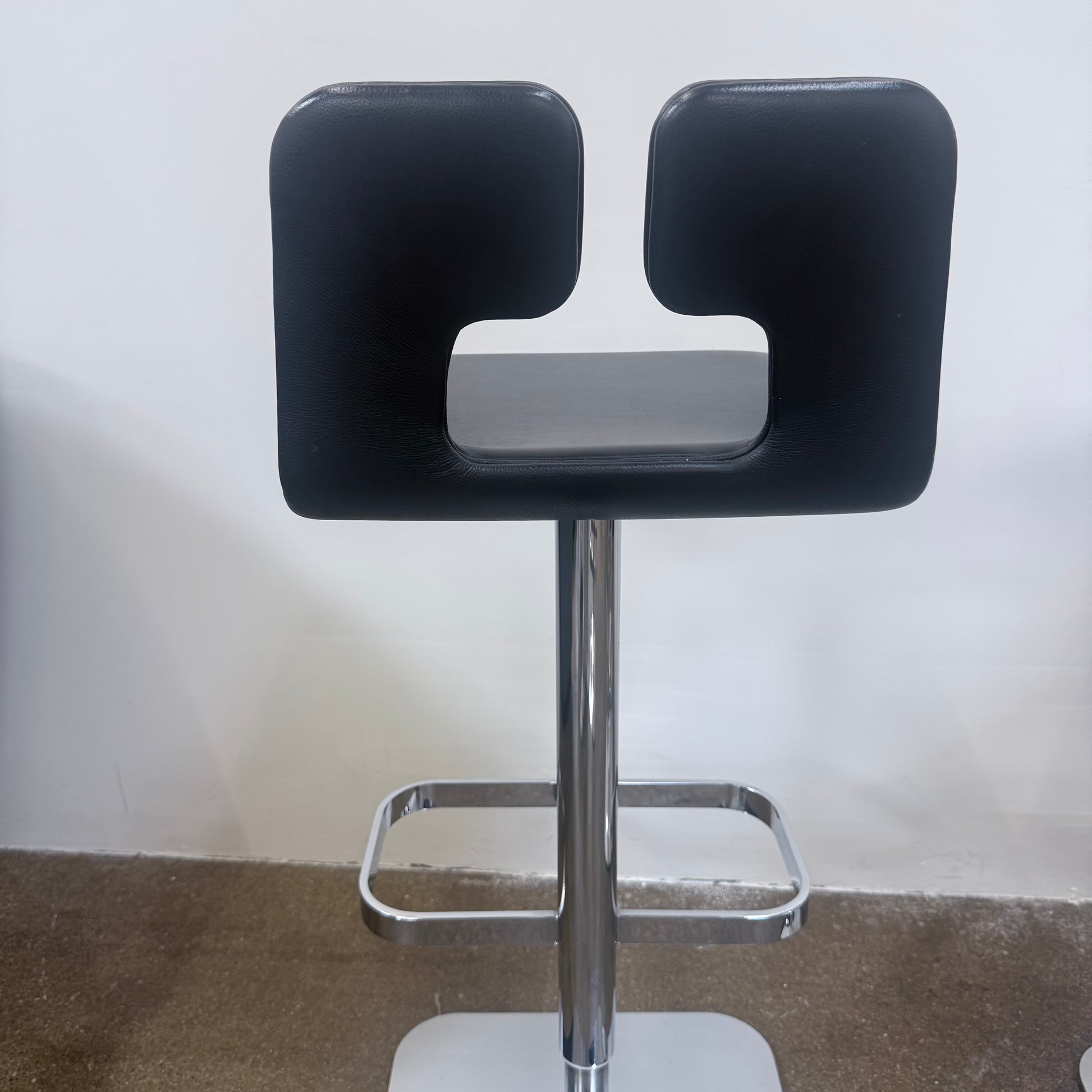 Set of 4 Poltrona Frau ALO Revolving Counter Height Stools in modern gray with square chrome bases are lined up against a white wall on a concrete floor, adding sleek Poltrona Frau style.