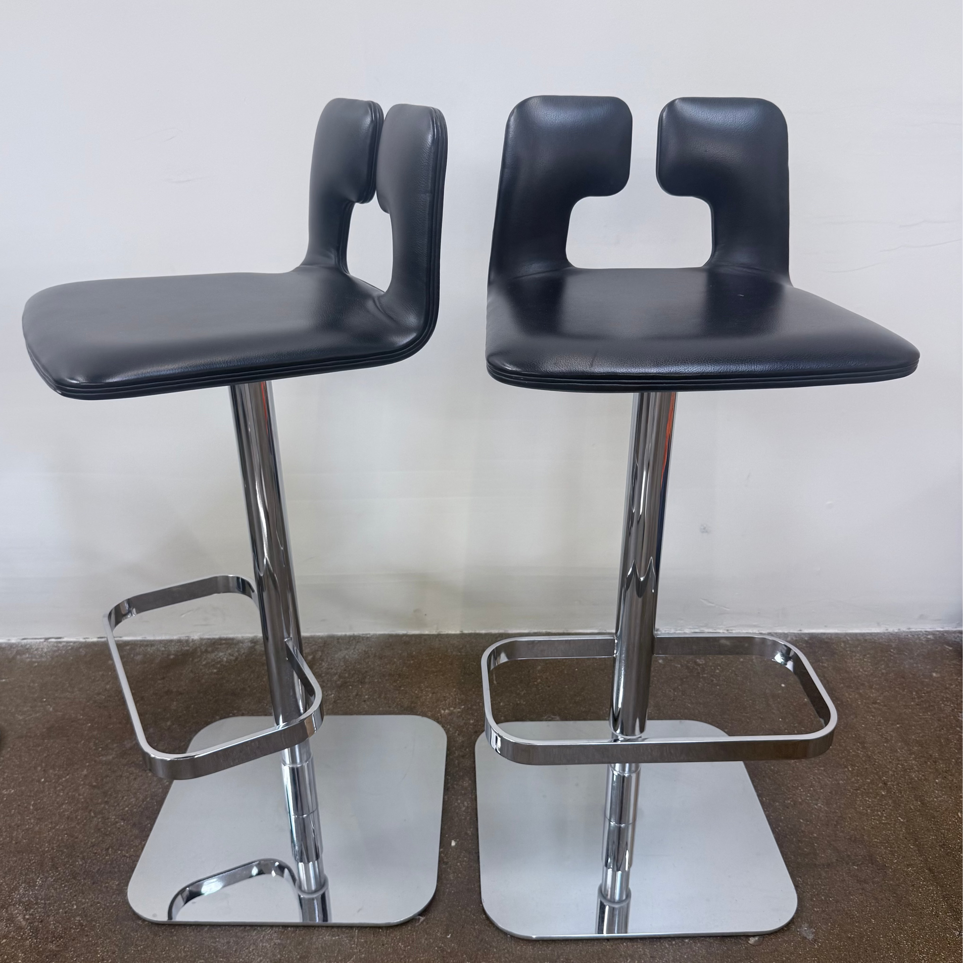 Set of 4 Poltrona Frau ALO Revolving Counter Height Stools in modern gray with square chrome bases are lined up against a white wall on a concrete floor, adding sleek Poltrona Frau style.