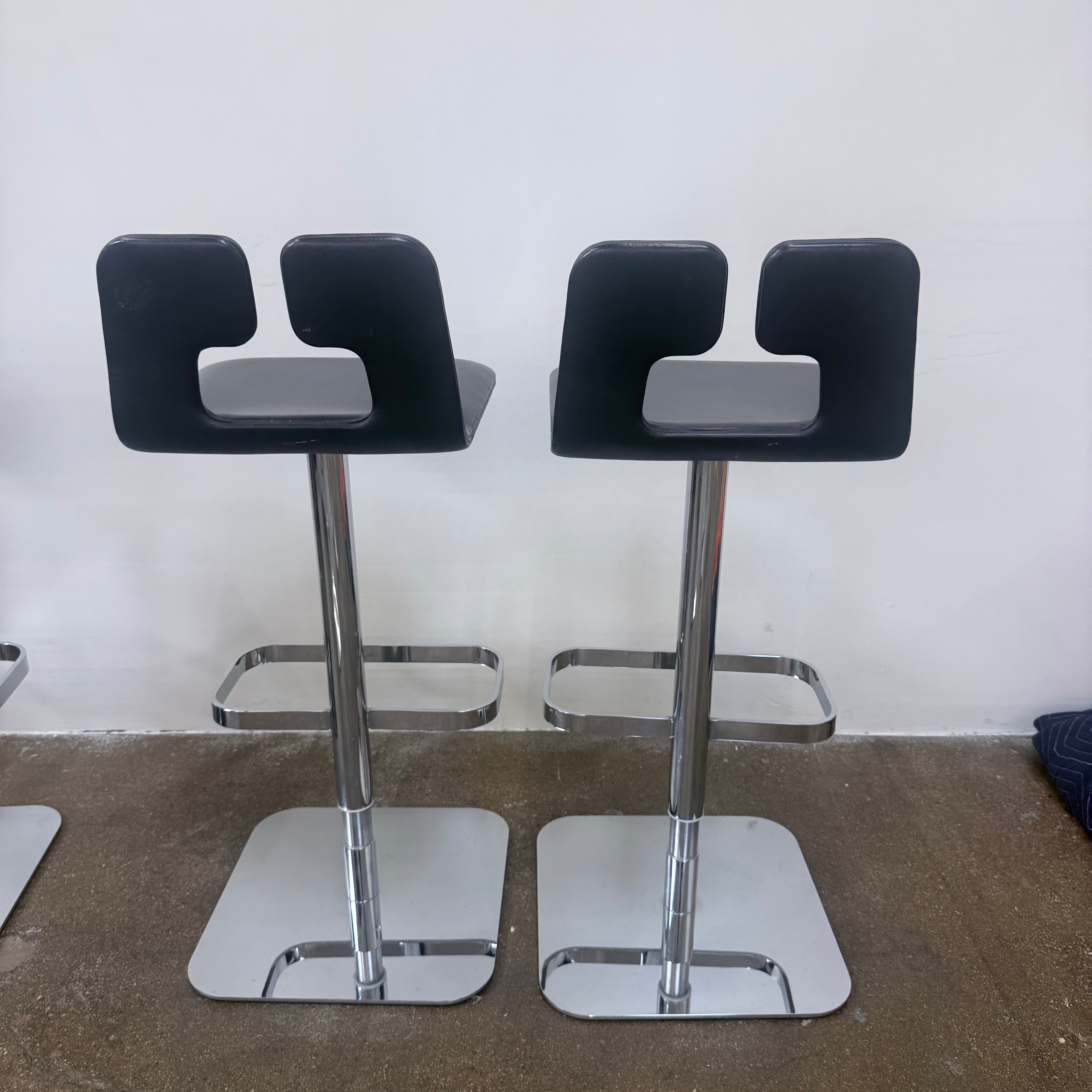 Set of 4 Poltrona Frau ALO Revolving Counter Height Stools in modern gray with square chrome bases are lined up against a white wall on a concrete floor, adding sleek Poltrona Frau style.