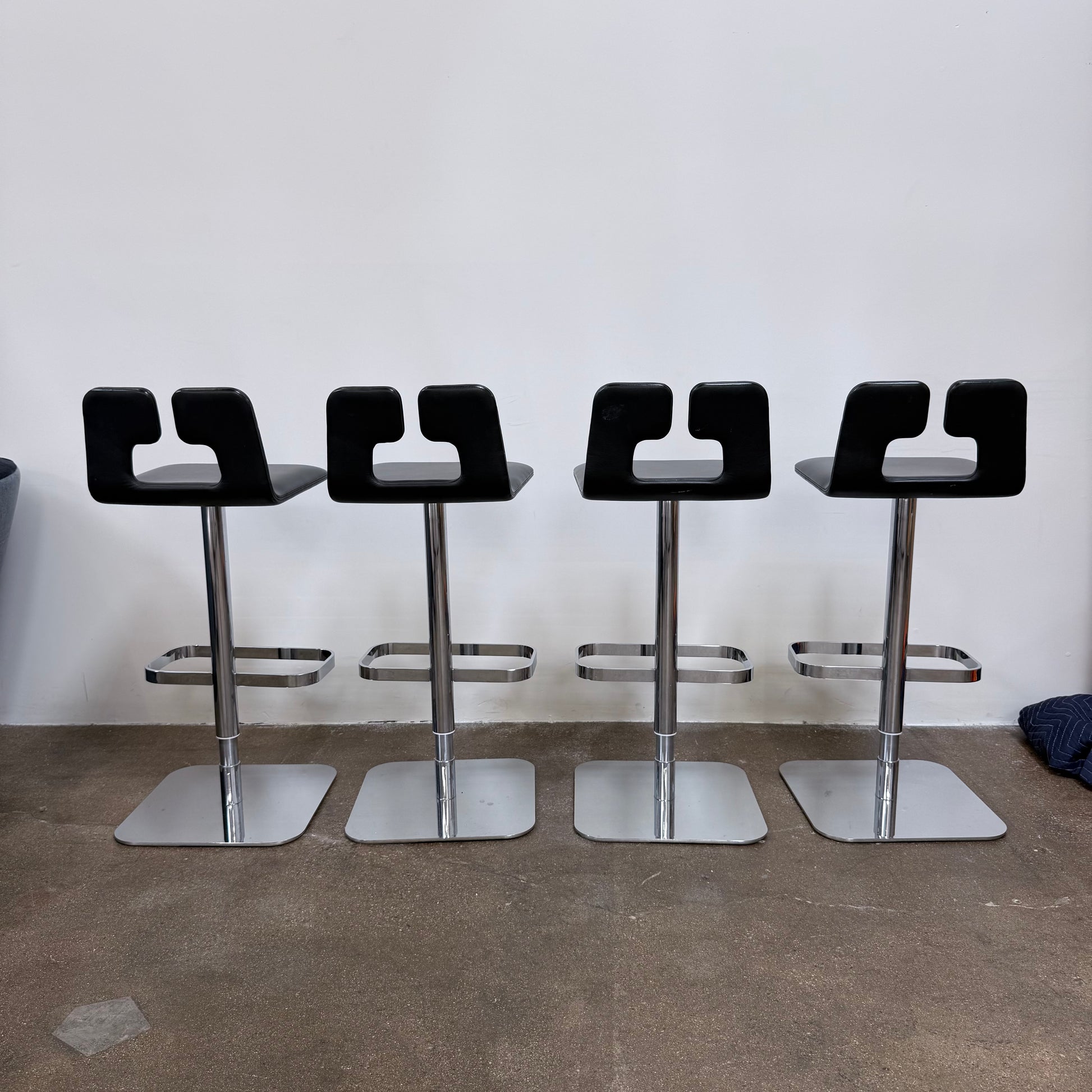 Four Poltrona Frau ALO Revolving Counter Height Adjustable Stools in black leather with chrome bases are arranged in a row, highlighting their modern design against a white background.