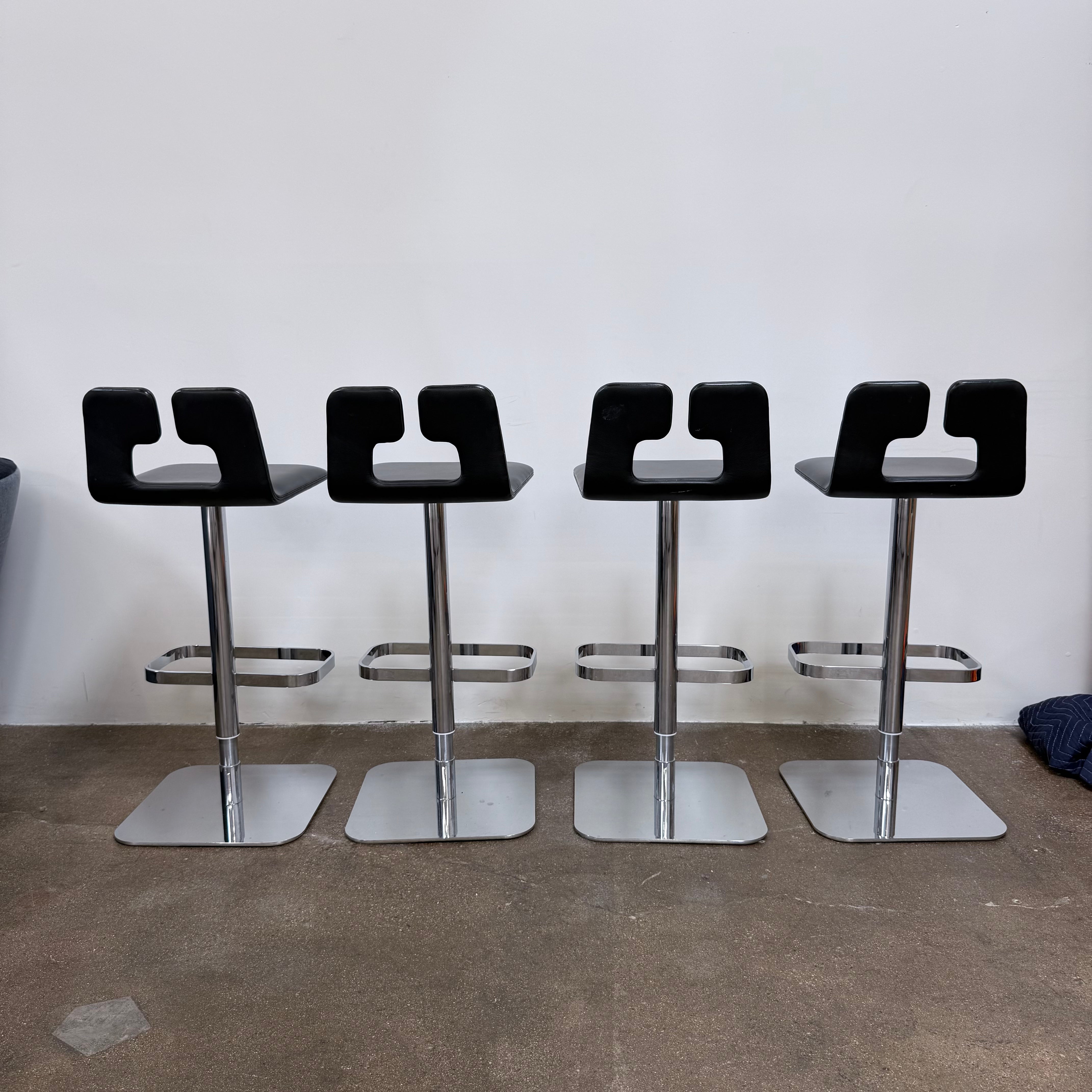 Four Poltrona Frau ALO Revolving Counter Height Adjustable Stools in black leather with chrome bases are arranged in a row, highlighting their modern design against a white background.