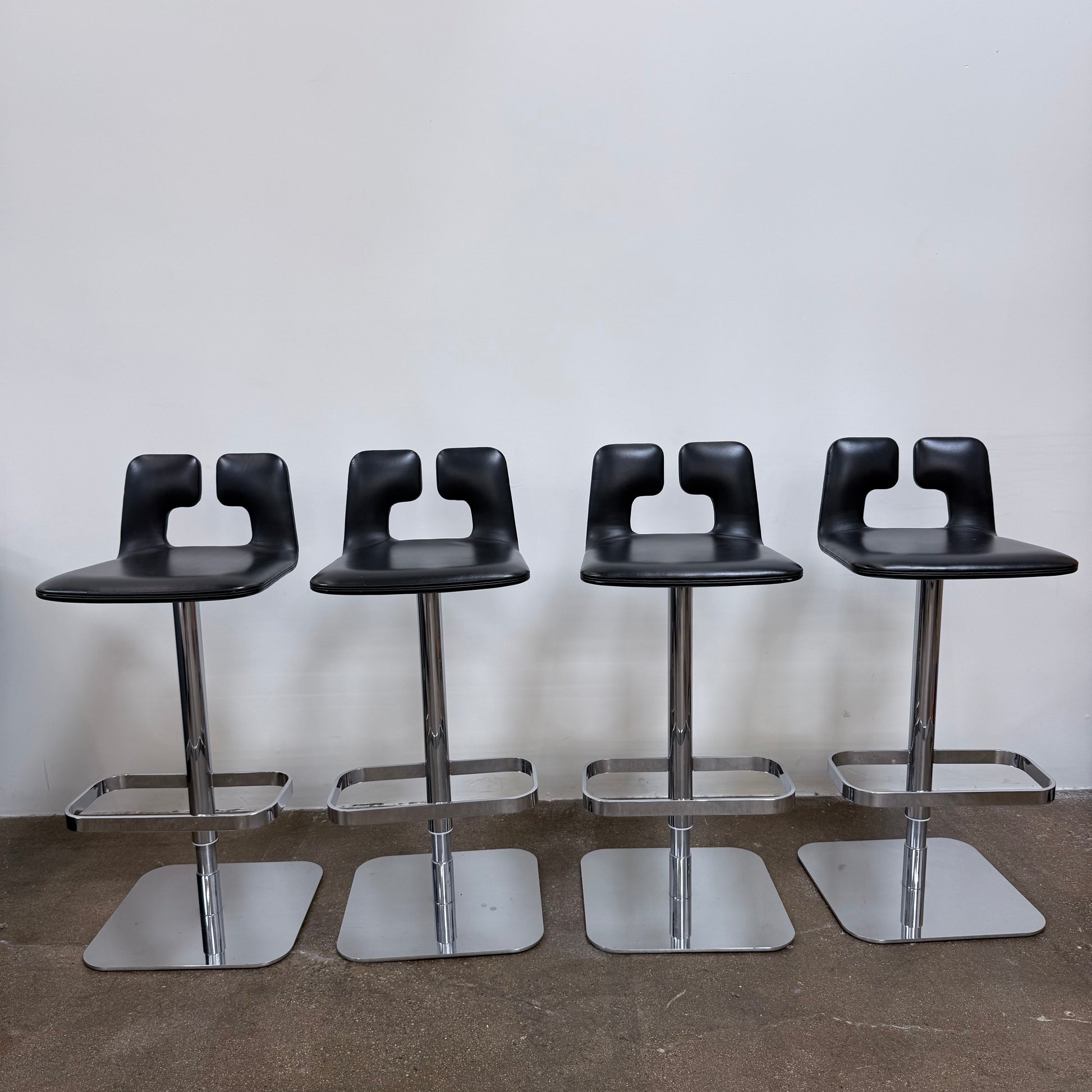 Four Poltrona Frau ALO Revolving Counter Height Adjustable Stools in black leather with chrome bases are arranged in a row, highlighting their modern design against a white background.