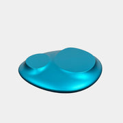 The Roche Bobois cute cut | XXM Cocktail Table by Roche Bobois is a smooth, metallic blue piece with rounded, uneven surfaces, displayed on a brown concrete floor against a white wall in contemporary style.