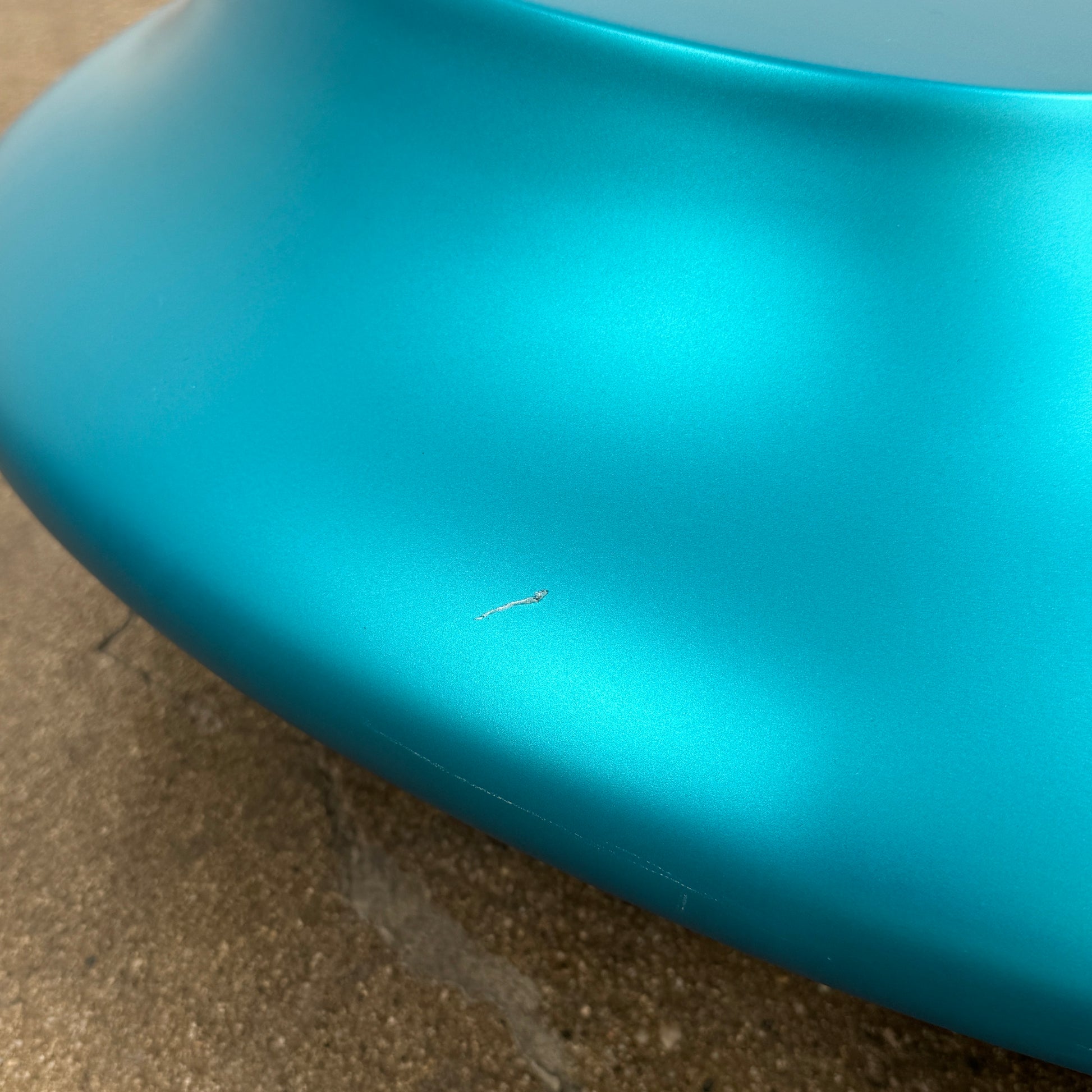 The Roche Bobois cute cut | XXM Cocktail Table by Roche Bobois is a smooth, metallic blue piece with rounded, uneven surfaces, displayed on a brown concrete floor against a white wall in contemporary style.
