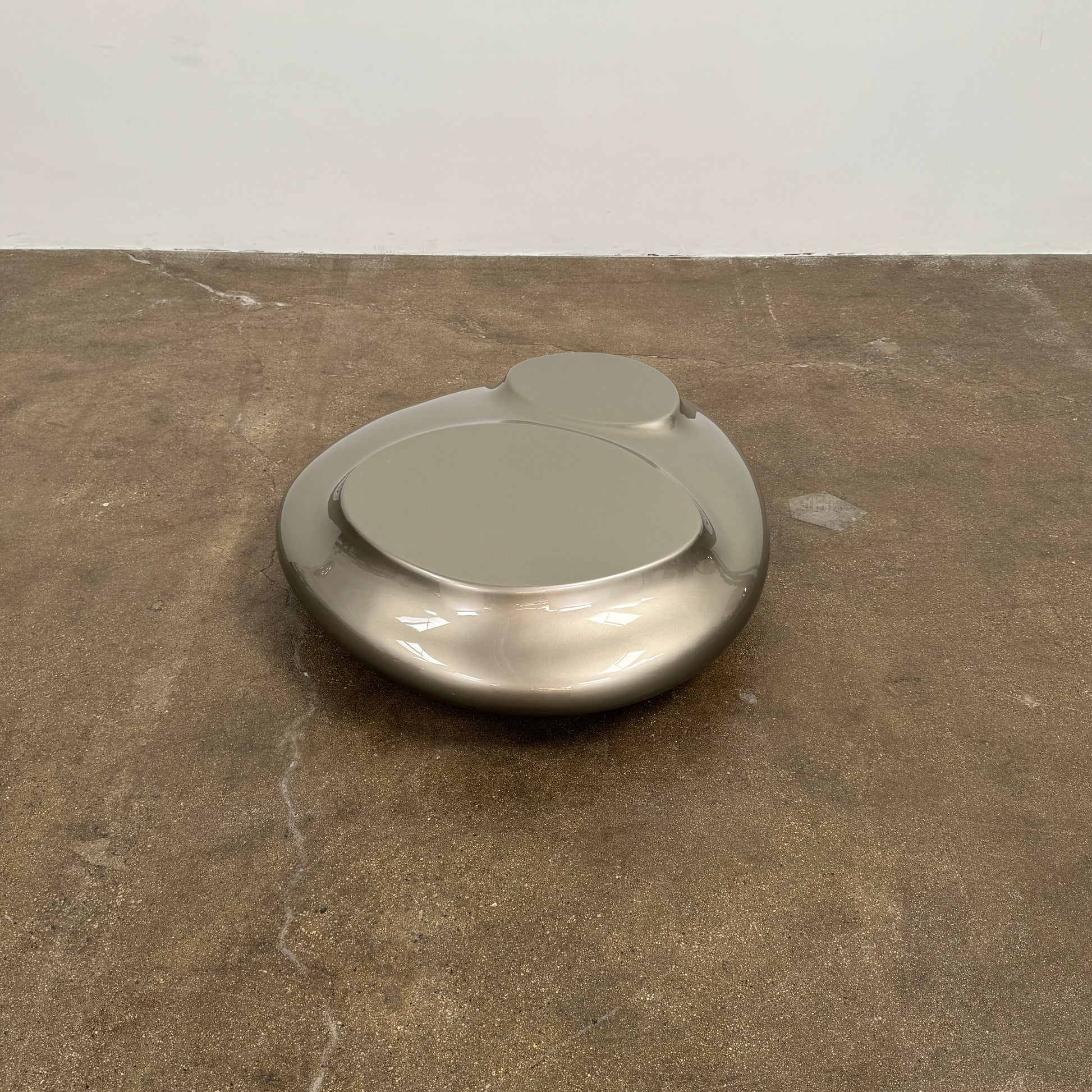 A metallic, smooth, irregularly shaped object with three raised sections on a white background—evoking the sleek Roche Bobois Cute Cut | XXM Cocktail Table, ideal for modern interiors.