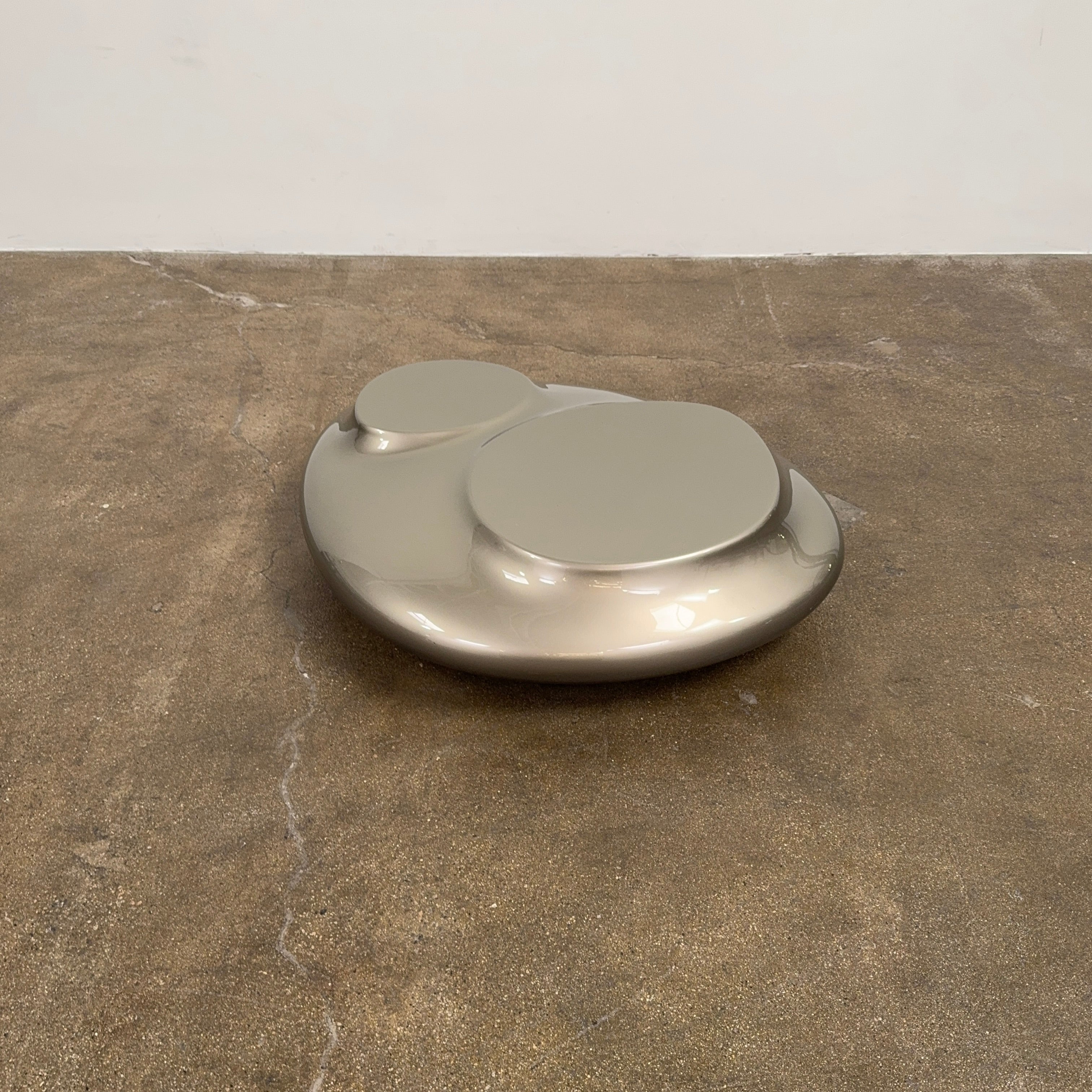 A metallic, smooth, irregularly shaped object with three raised sections on a white background—evoking the sleek Roche Bobois Cute Cut | XXM Cocktail Table, ideal for modern interiors.