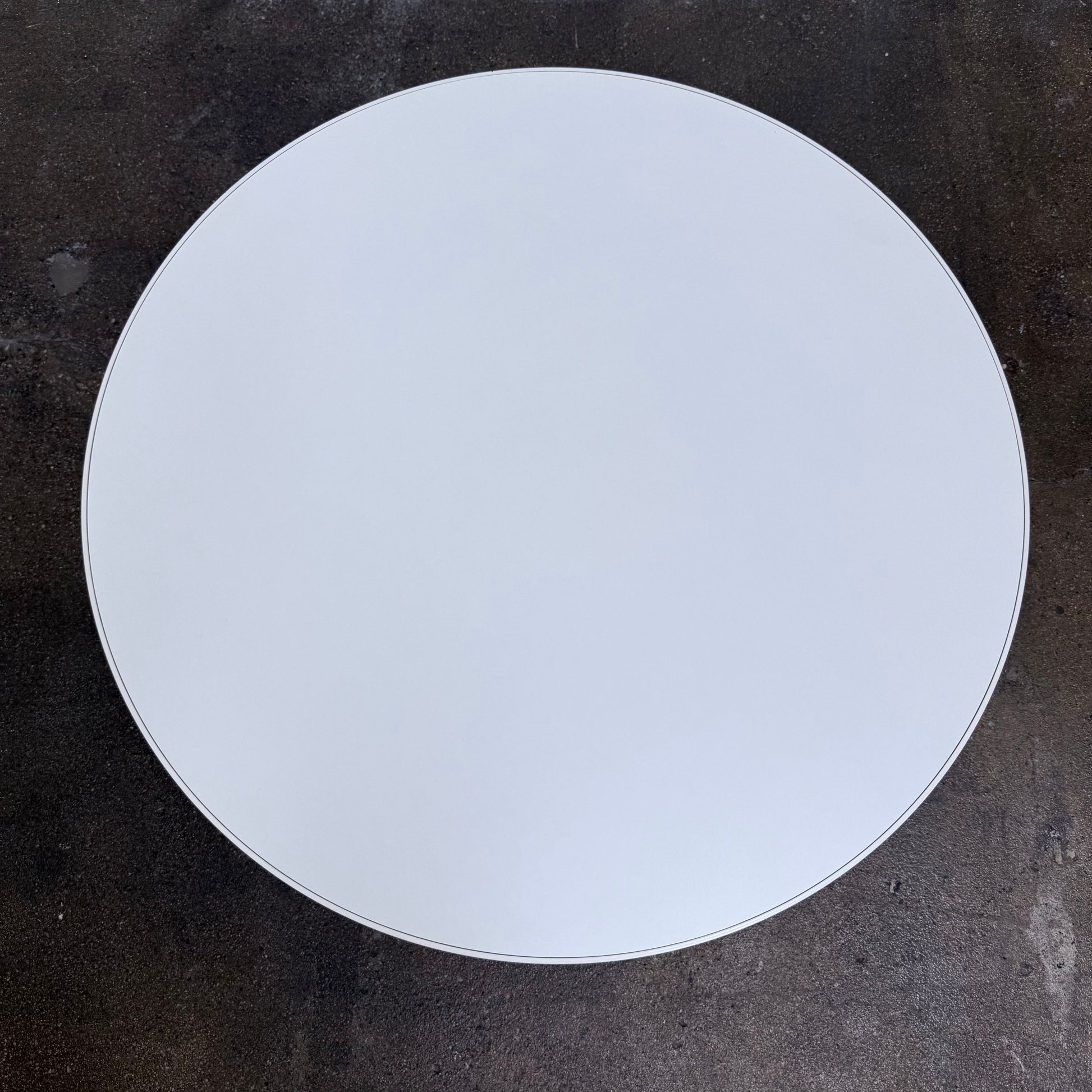 A round Tacchini Cage Coffee Table, White by Tacchini with thin metal legs stands on a plain gray concrete floor against a blank wall.