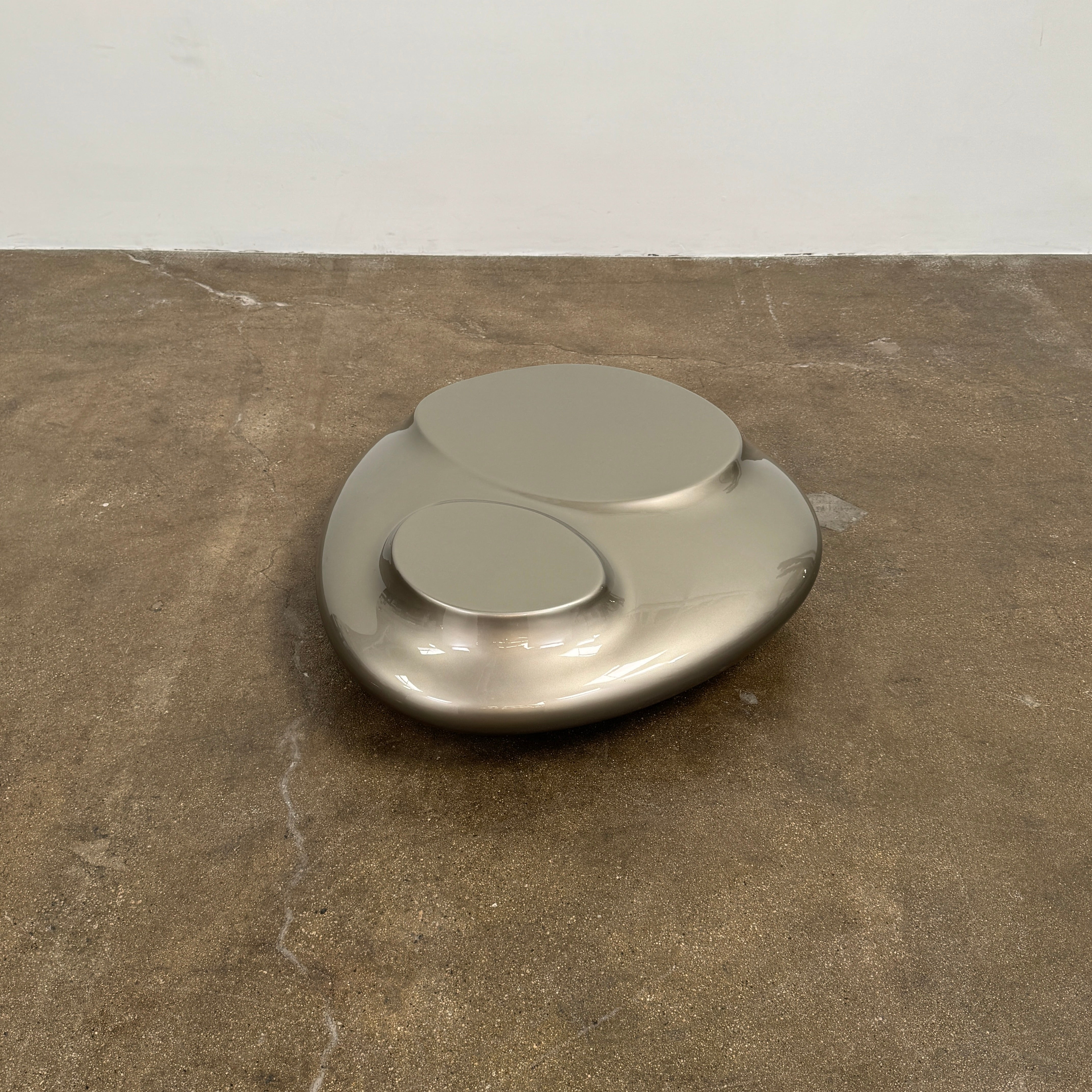 A metallic, smooth, irregularly shaped object with three raised sections on a white background—evoking the sleek Roche Bobois Cute Cut | XXM Cocktail Table, ideal for modern interiors.