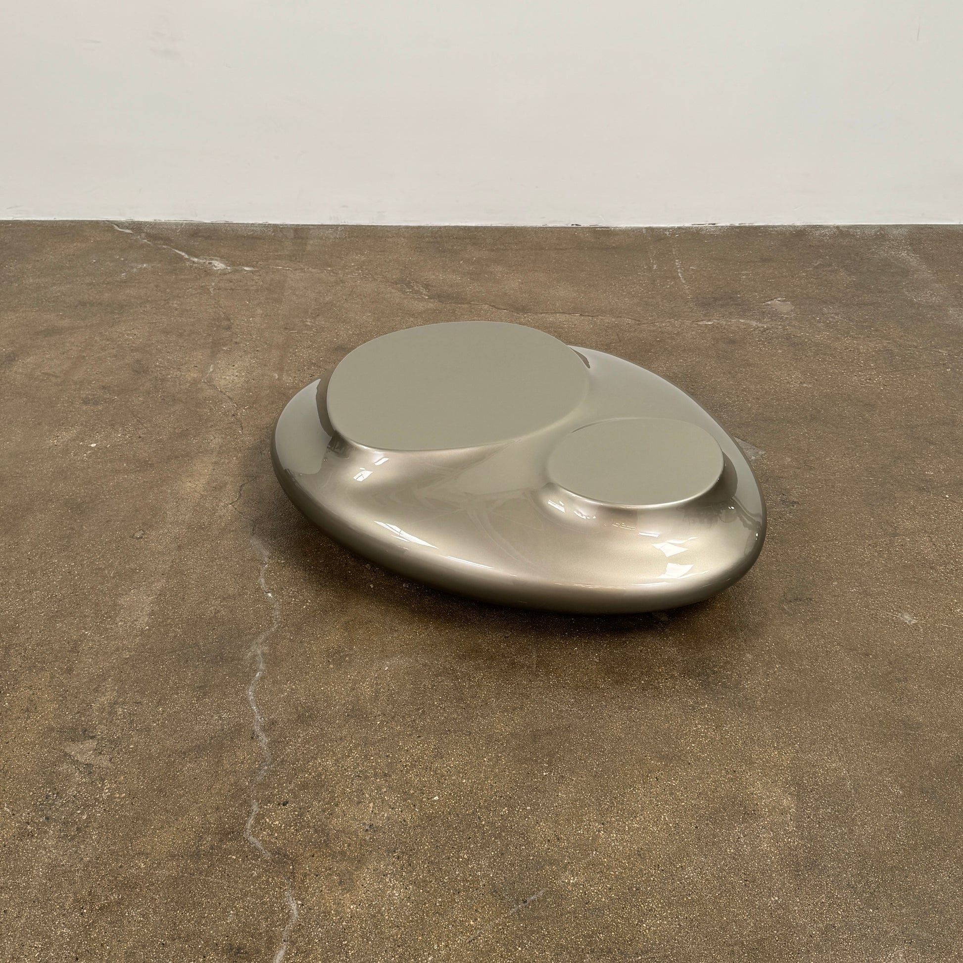 A metallic, smooth, irregularly shaped object with three raised sections on a white background—evoking the sleek Roche Bobois Cute Cut | XXM Cocktail Table, ideal for modern interiors.