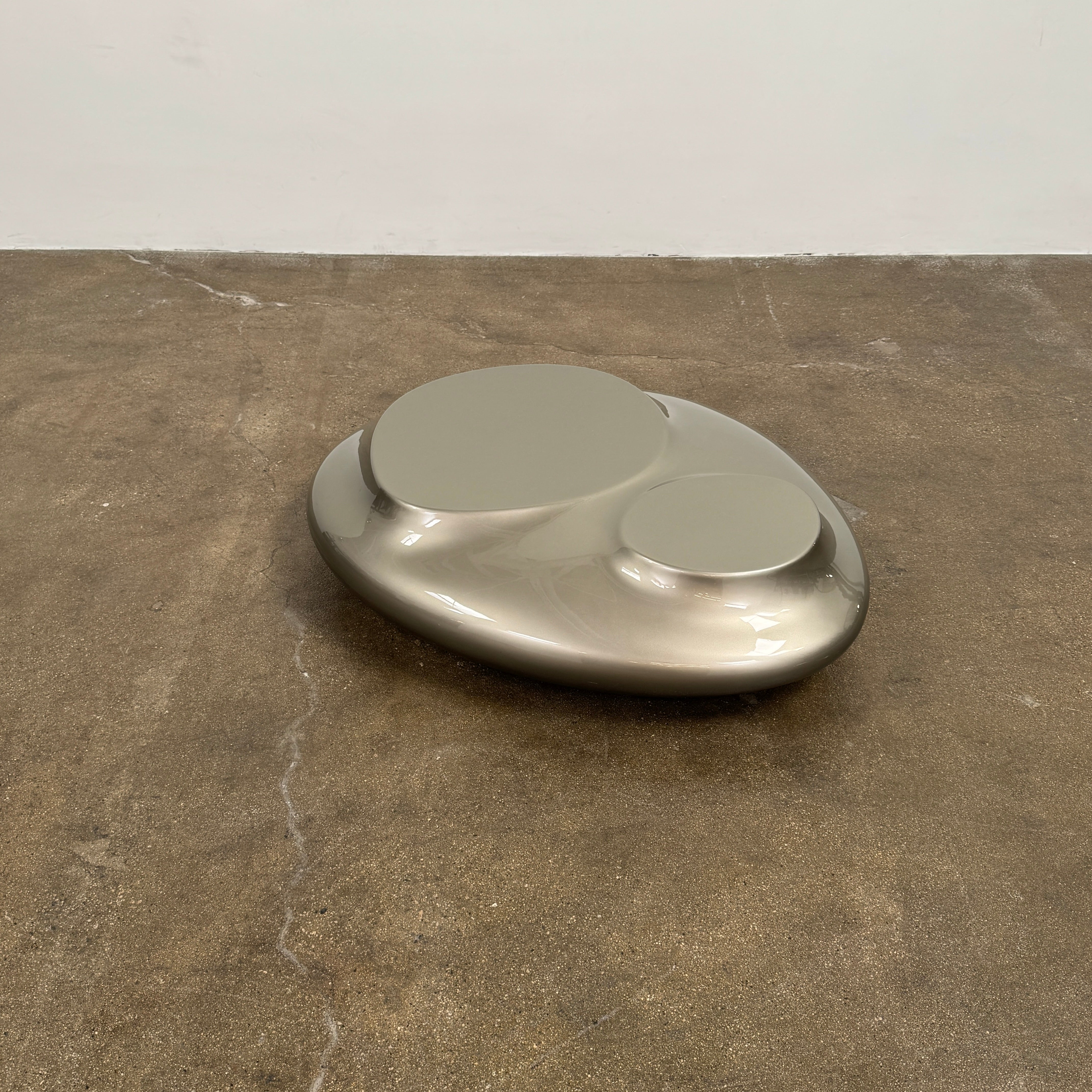 A metallic, smooth, irregularly shaped object with three raised sections on a white background—evoking the sleek Roche Bobois Cute Cut | XXM Cocktail Table, ideal for modern interiors.