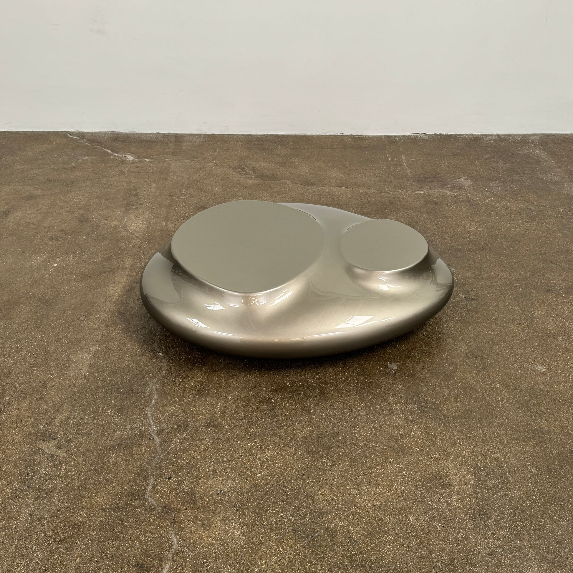 A metallic, smooth, irregularly shaped object with three raised sections on a white background—evoking the sleek Roche Bobois Cute Cut | XXM Cocktail Table, ideal for modern interiors.
