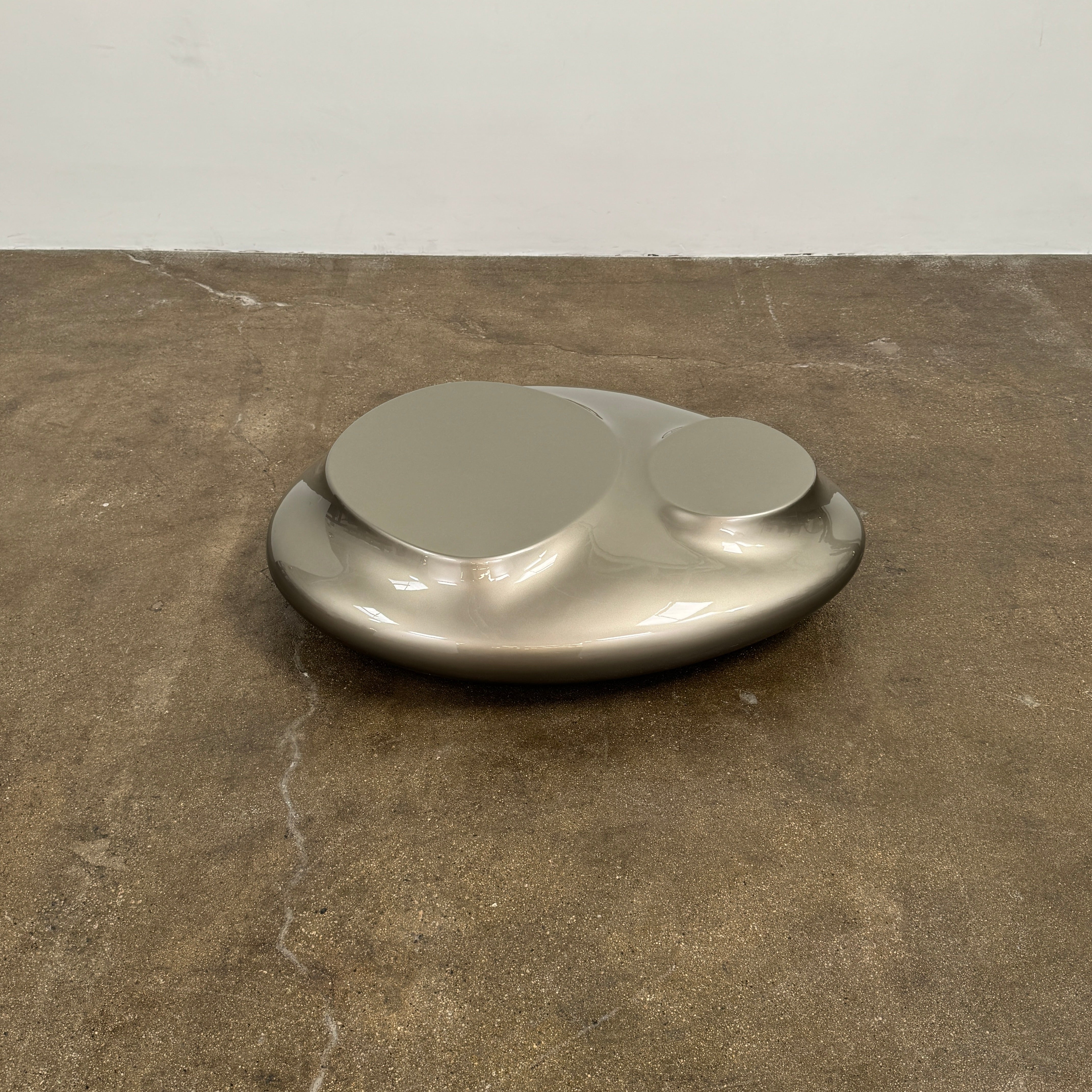 A metallic, smooth, irregularly shaped object with three raised sections on a white background—evoking the sleek Roche Bobois Cute Cut | XXM Cocktail Table, ideal for modern interiors.
