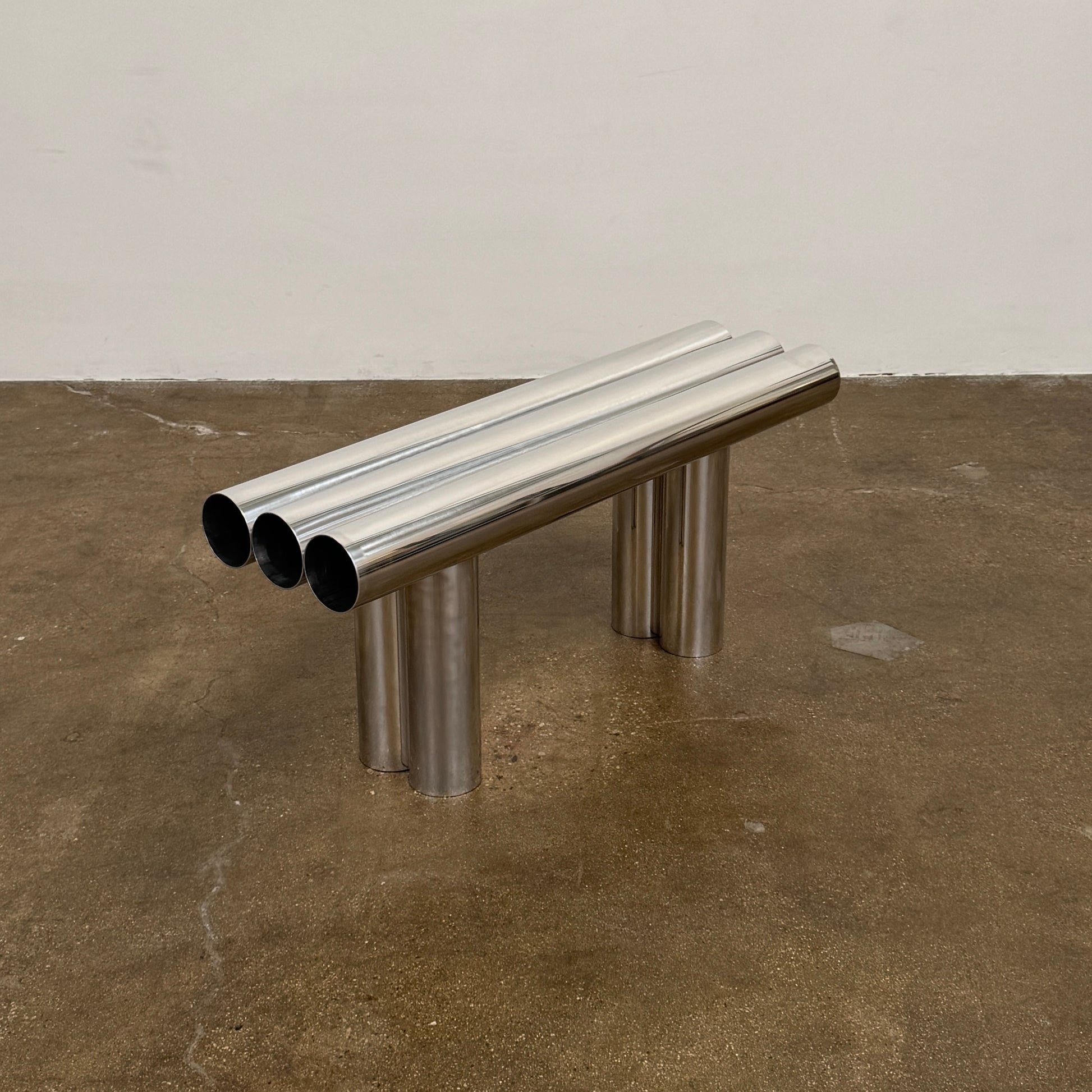 The Axel Chay Septem Bench from Modern Resale features a modern design with three polished aluminum cylinders as the seat, supported by three angled cylindrical legs, evoking classic irrigation pipe benches.