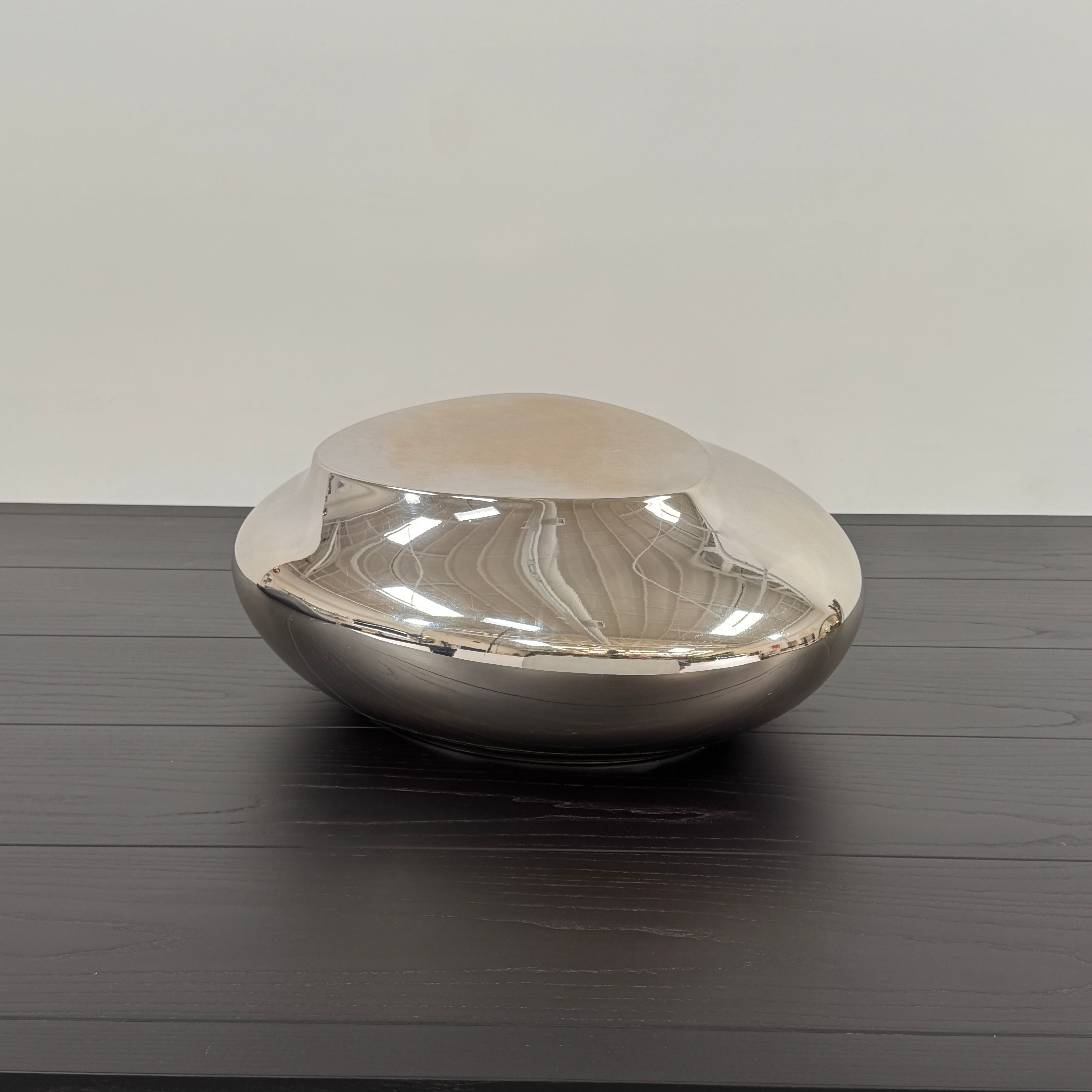 The Roche Bobois cute cut | XXS Cocktail table, with its round, reflective silver surface and smooth, unique shape, stands elegantly against a plain white background—an ideal accent for modern interiors.