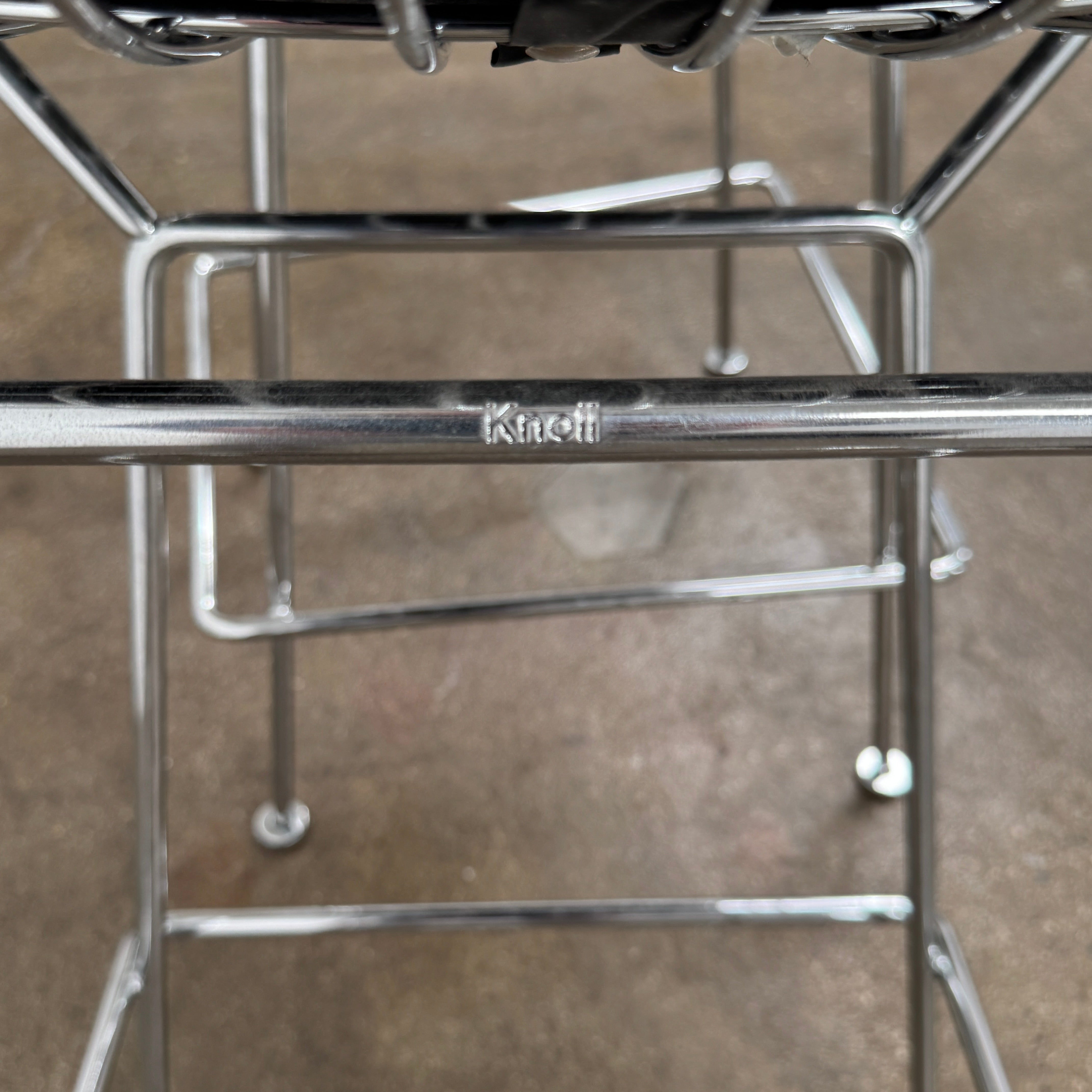A set of two Knoll Bertoia Counter Stools by Knoll, with light seat cushions, are placed side by side on a brown concrete floor against a plain white wall.