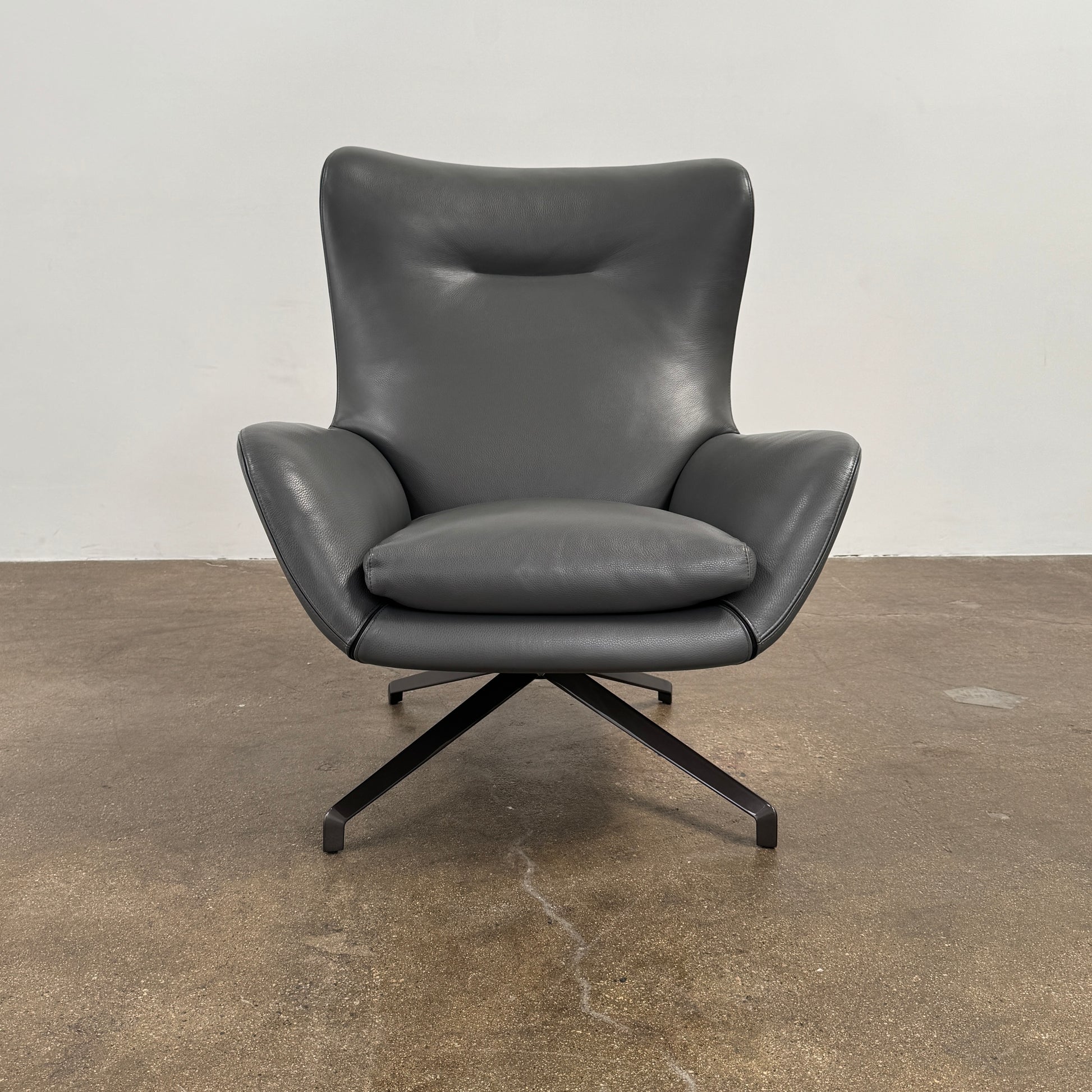 The Minotti Jensen Swivel Armchair features black leather upholstery, a high backrest, and angled metal legs by Minotti, displayed against a plain white background.