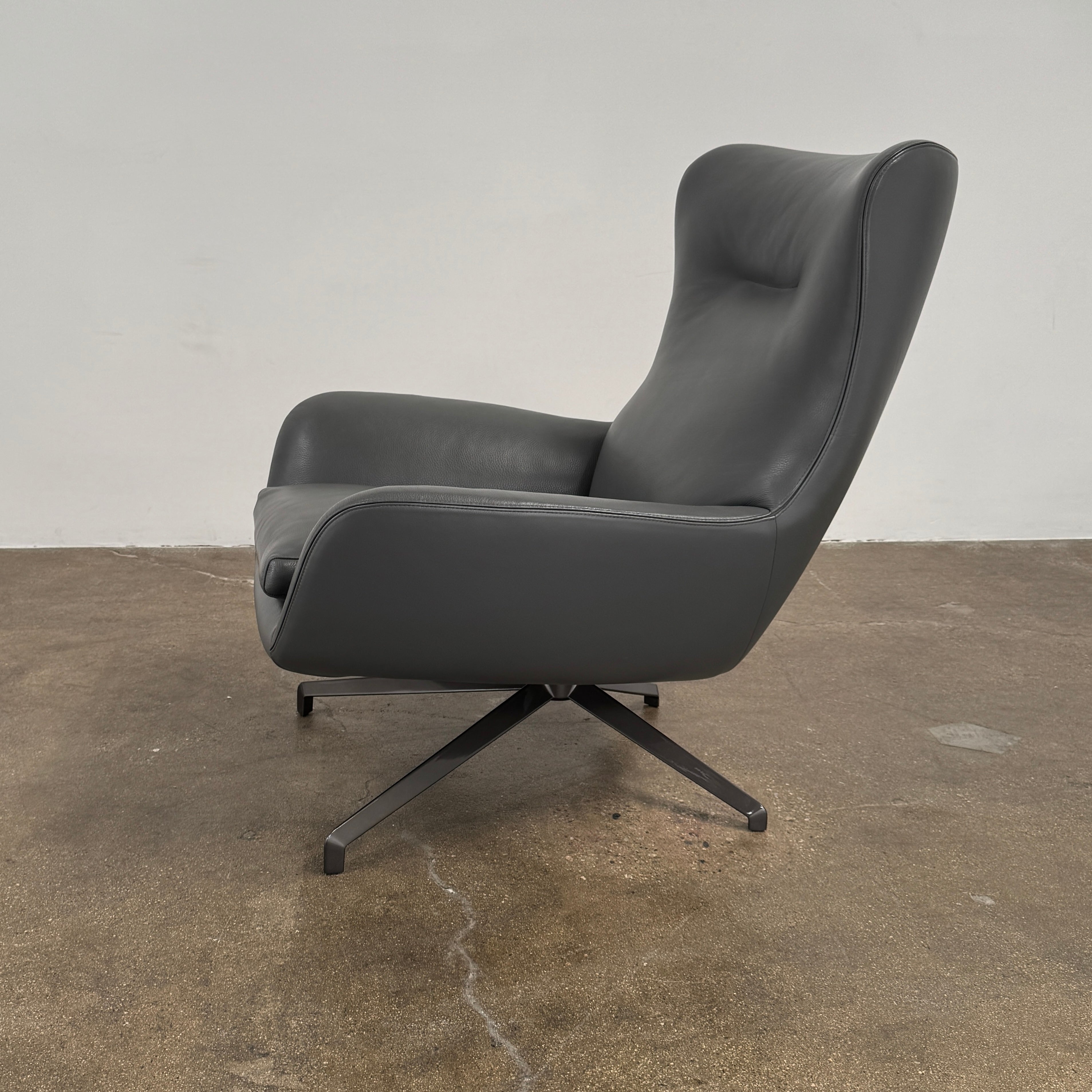 The Minotti Jensen Swivel Armchair features black leather upholstery, a high backrest, and angled metal legs by Minotti, displayed against a plain white background.