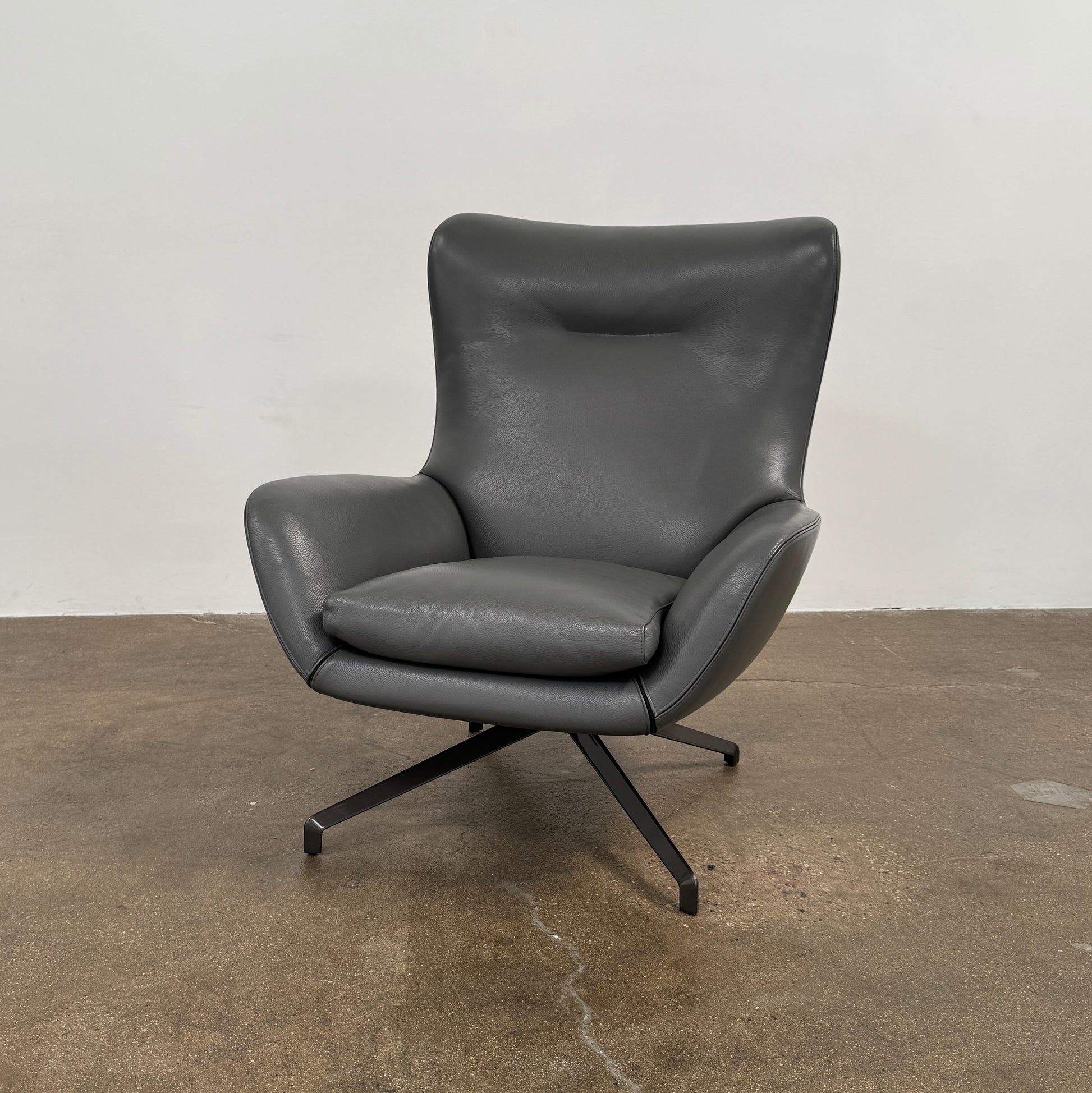 The Minotti Jensen Swivel Armchair features black leather upholstery, a high backrest, and angled metal legs by Minotti, displayed against a plain white background.