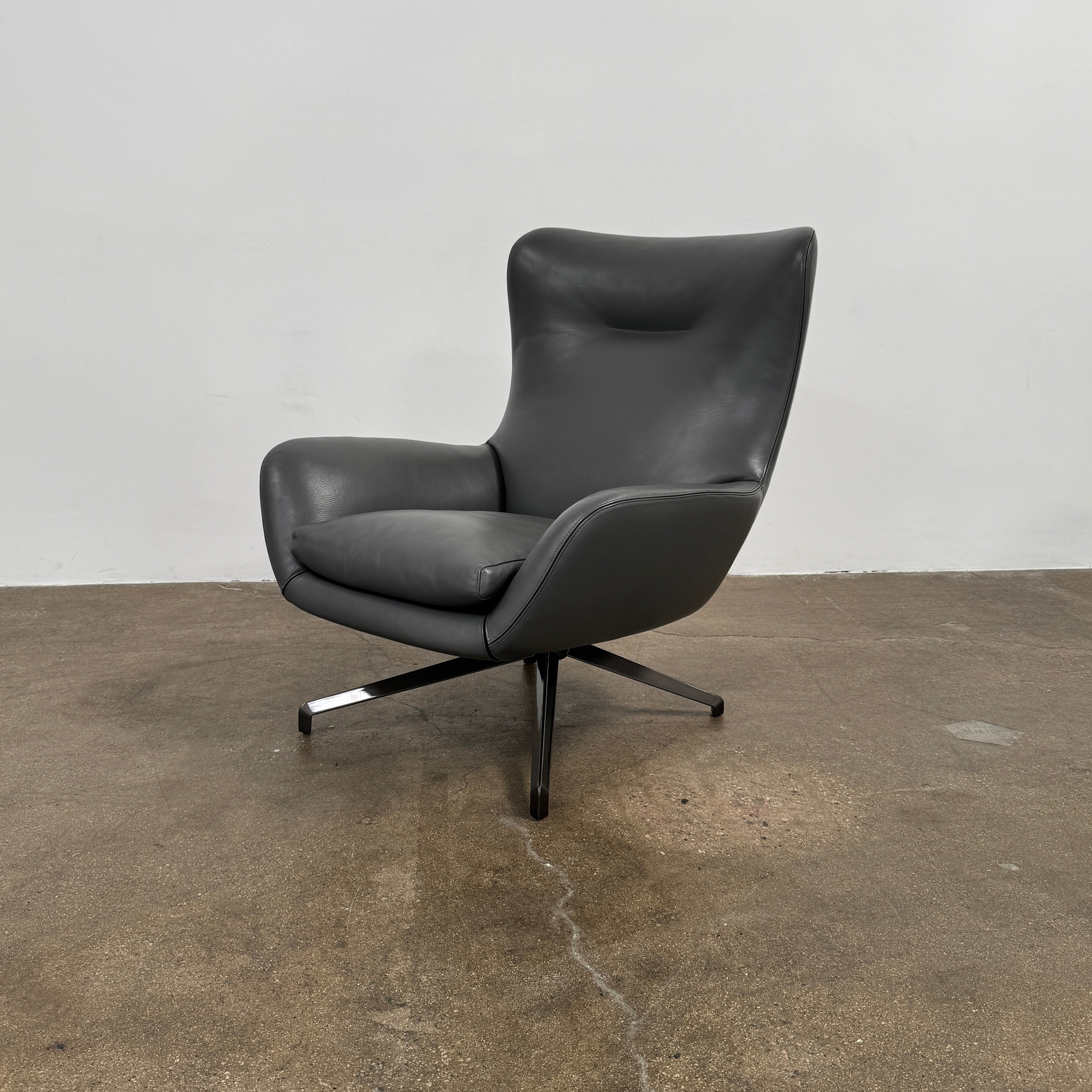 The Minotti Jensen Swivel Armchair features black leather upholstery, a high backrest, and angled metal legs by Minotti, displayed against a plain white background.