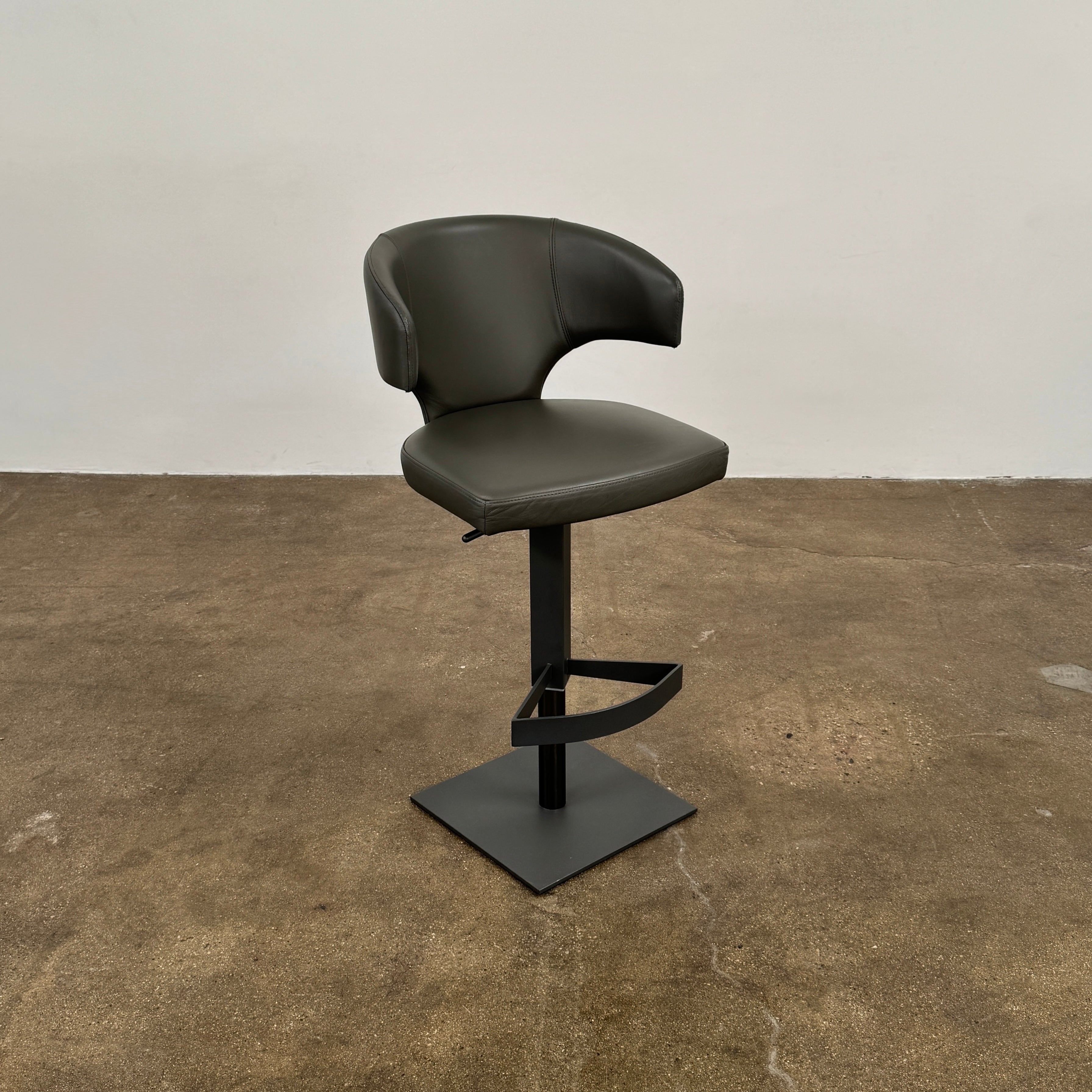 The Cantoni Wing Barstool by Cantoni features a modern black swivel design with a metal base, set on a brown concrete floor against a plain white wall.