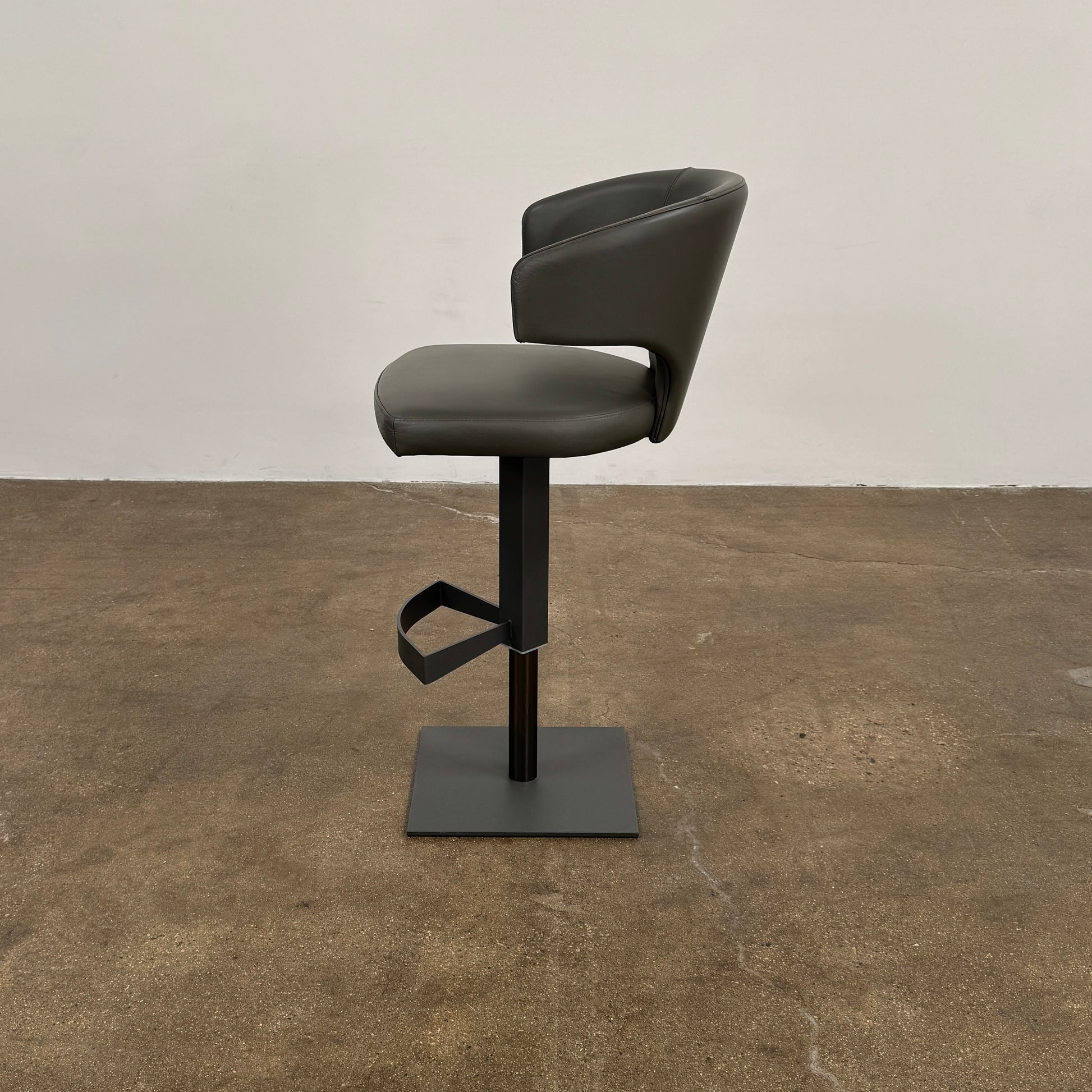 The Cantoni Wing Barstool by Cantoni features a modern black swivel design with a metal base, set on a brown concrete floor against a plain white wall.