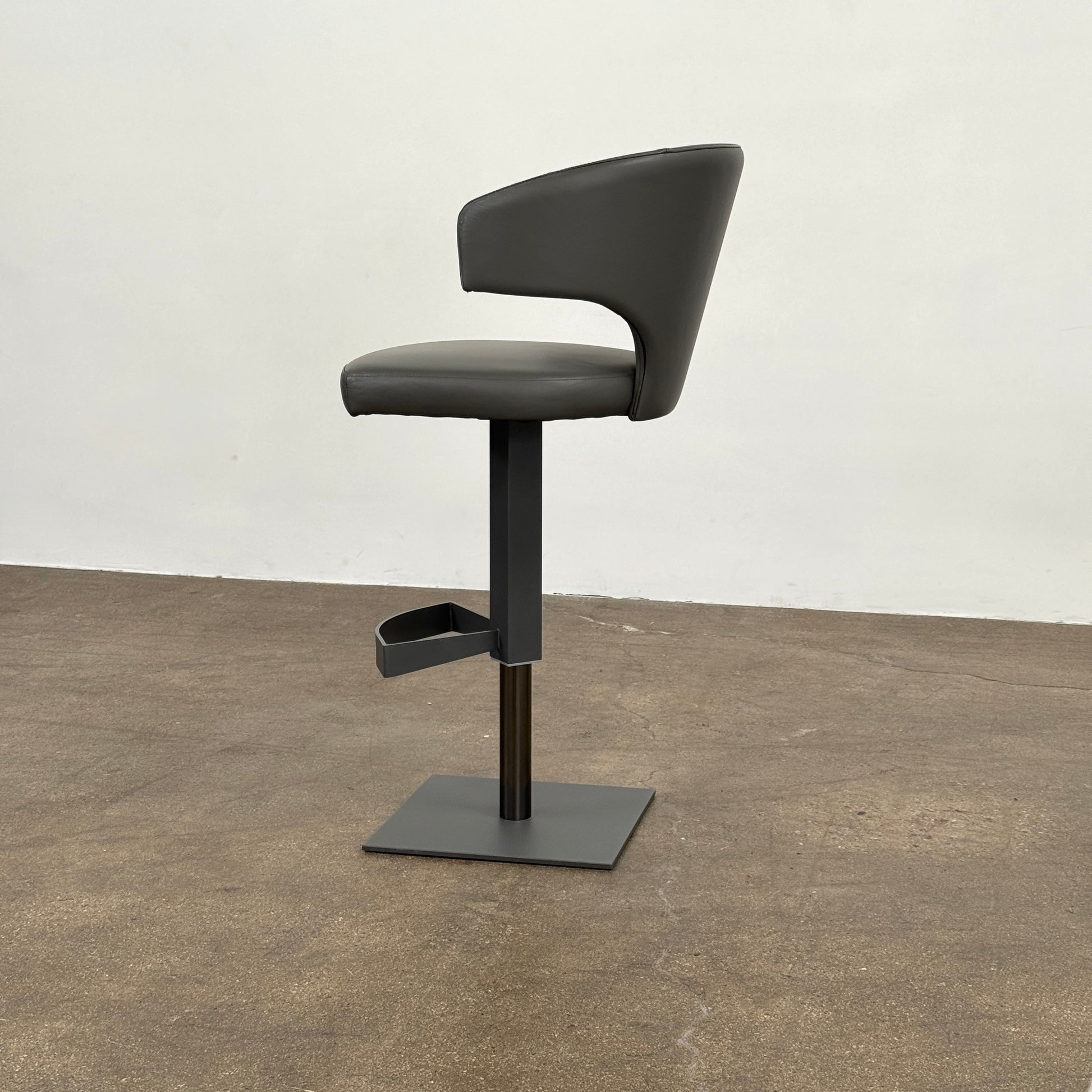 The Cantoni Wing Barstool by Cantoni features a modern black swivel design with a metal base, set on a brown concrete floor against a plain white wall.